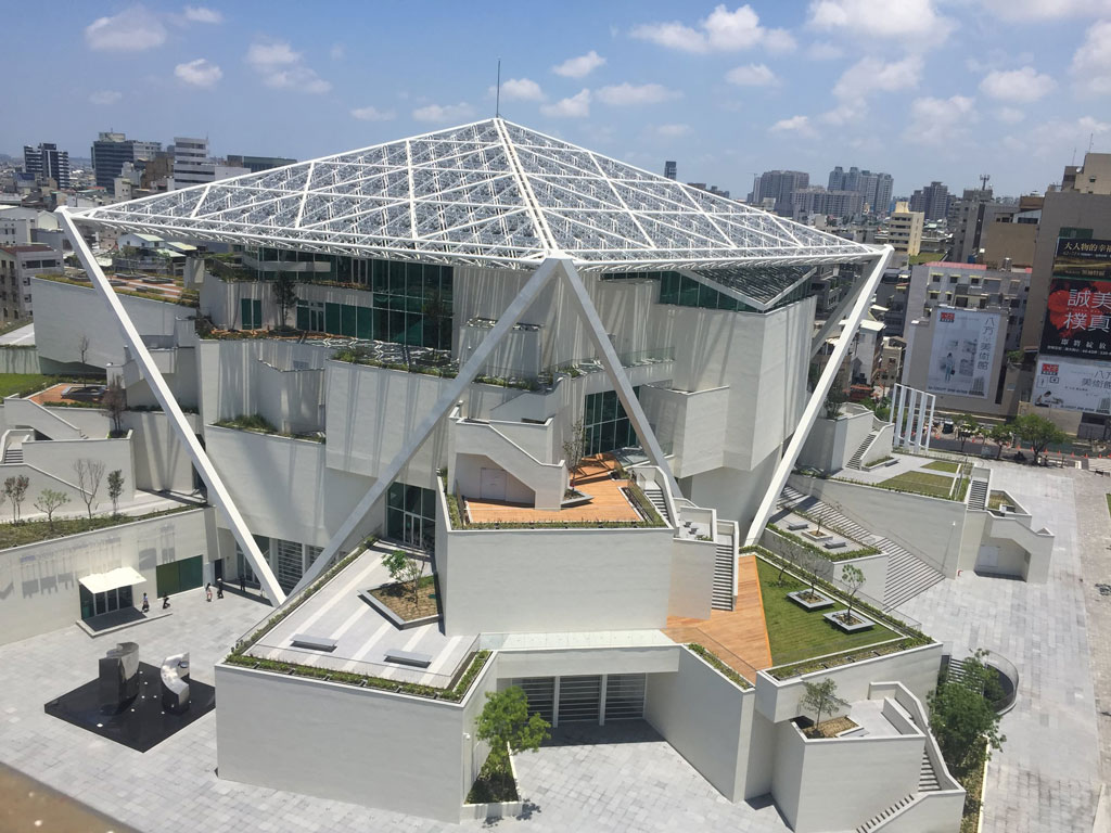 台南市立美術館2館由日本建築師阪茂和石昭永建築事務所合作設計，坐落於1920年代的台南神社所在地，過去這裡曾建有海東書院、台南博物館，還有迄今仍保留的孔廟，可謂台南的文教中心。整體運用不同角度盒子堆疊的意象，為建築打造不少半戶外的空間，這種有遮蔭效果的戶外平台，不僅能阻擋日照直射，還能通風換氣，提供民眾更多欣賞周圍綠意的機會