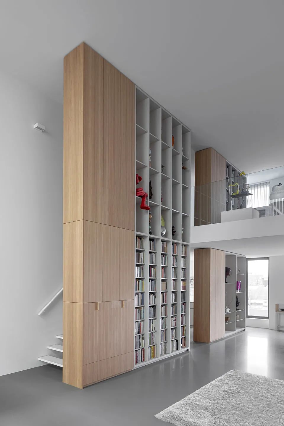 挑高空間內的木作書櫃，不只作為收納，也扮演類似牆壁的作用，背後以樓梯連結高低兩層