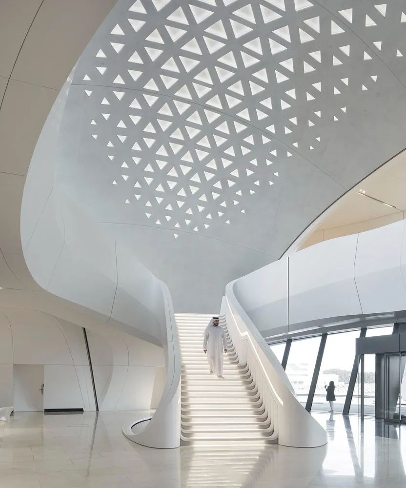 走入室內空間，設計延續了對於環境的解構，優雅反映了 Beeah 集團對可持續性和技術的關注，在建築物內定義了一片綠洲，將建築物外部的流暢設計語言向內延伸，位於中心的樓梯如同巨型雕塑般形塑出大器端景，波紋狀的踏板從上層延展而下，將複雜的幾何概念化為優美流暢的曲線造型