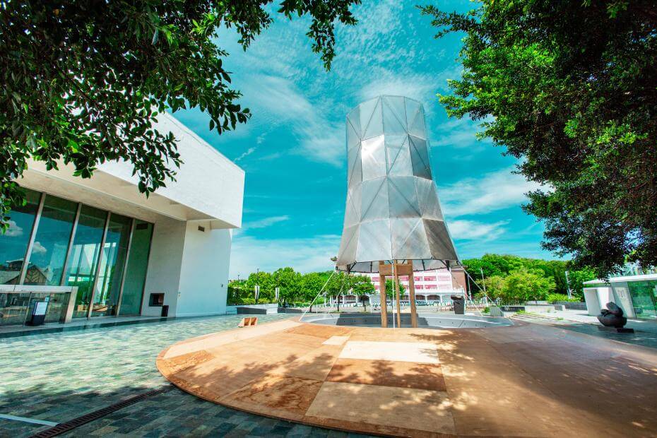 北美館第8屆X-site《爆炸容器》在建築外圍,以木構造緩坡製造出下沉式中央環形的類劇場空間,讓觀眾能從四面八方走進來,擁抱360度廣衾、毫無阻礙的觀看視野。除此之外,因建築體內部加裝了六條13米左右、4,000K偏黃的LED防水燈條,夜幕低垂時,並能製造出忽明忽滅的循環視覺效果,猶如斷電般,間接烘托出末日神秘感。讓人無論晴雨、白晝黑夜時造訪都別有意境。