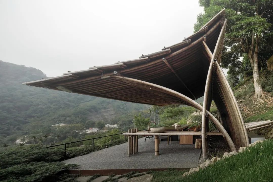 這座名為「竹亭」的建築完整地呈現了竹子的天然美感。透過高溫煙燻技術，竹材顯露出其獨特的褐色光澤，與周圍的山林和土地形成了完美的呼應