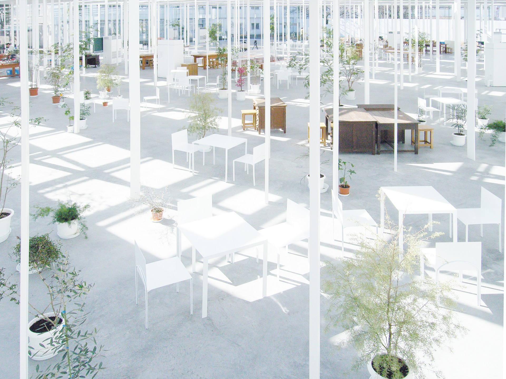 KAIT工房內，白色的家具與綠植點綴其間，室內的自然光線通過不規則排列的纖細鋼柱斑駁地投射在地面上。學生們在這些靈活可變的區塊中勾畫創意，無形的界線讓思緒自由飛揚。石上純也的這番設計，不僅促進學習與交流，更在這些交錯的陰影中訴說著靜謐與和諧的詩篇