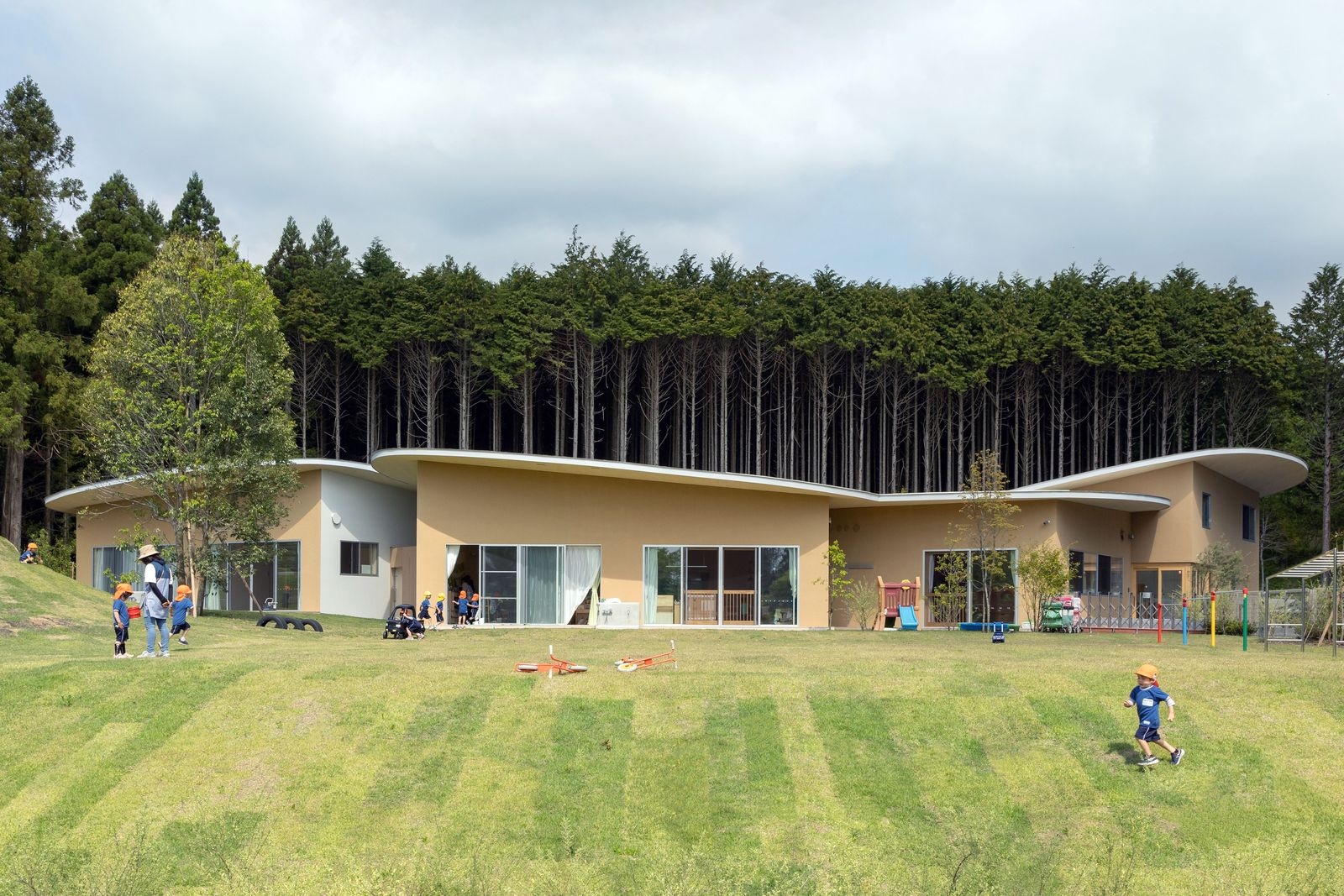 與富士山共舞的兒童樂園!靜岡縣「高嶺の森のこども園」幼兒園:讓孩子在四季更迭中感受自然的美麗/山下貴成建築設計事務所 設計獨特的園舍與周圍的森林相呼應。這裡的孩子們在廣闊的綠地上自由奔跑,享受著無拘無束的童年時光。園舍的建築形式優美,屋頂曲線與地形契合,內部多功能廳與各教室之間的連接巧妙,讓每個角落都充滿歡樂的氣息