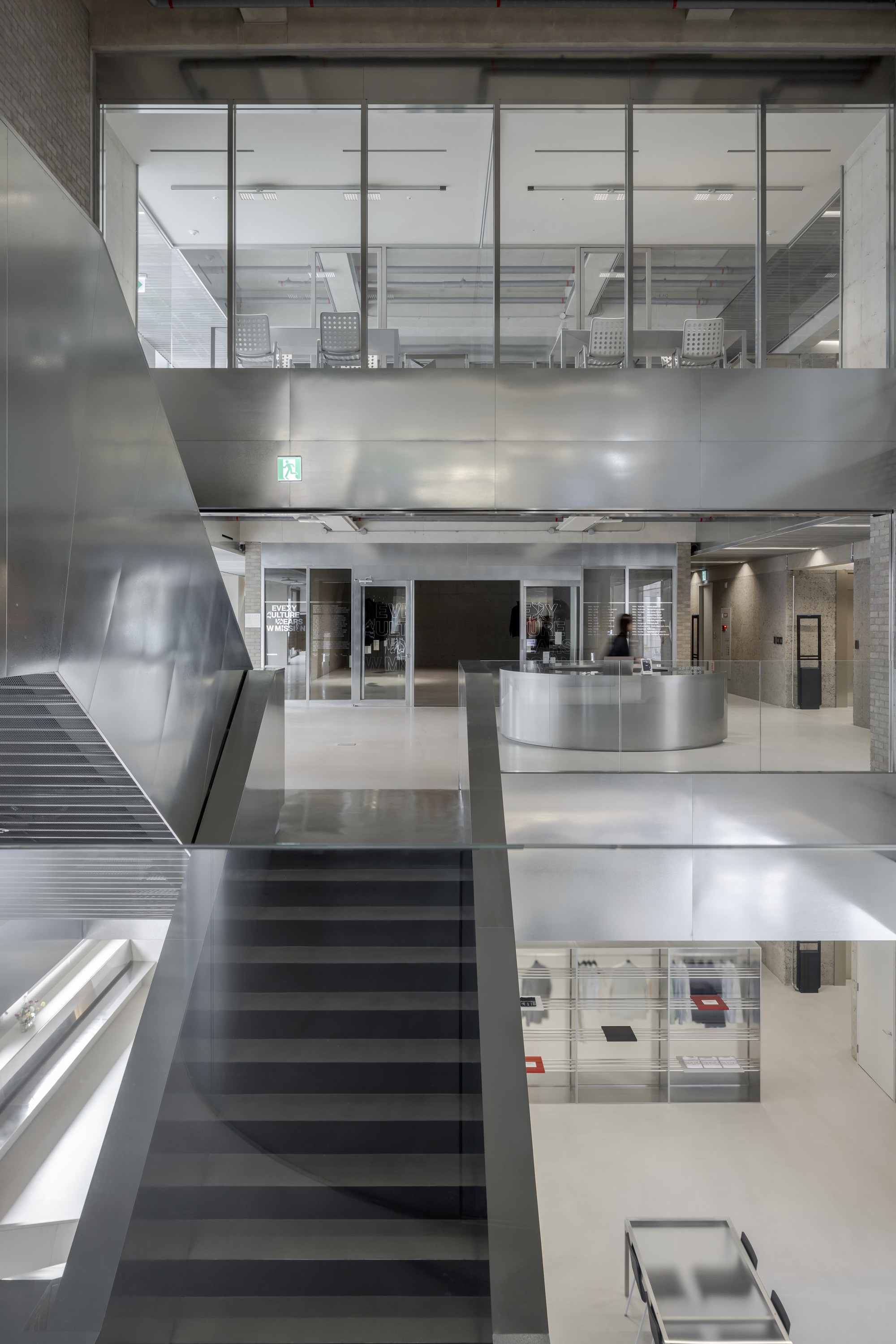 林友寒設計的W-Mission企業總部以銀色金屬打造的挑高空間，搭配簡潔俐落的線條，營造出未來感十足的氛圍，寬敞樓梯串聯各樓層，自然光線透過大面玻璃窗灑落，與金屬光澤相互輝映，完美呈現W-Mission的時尚前衛精神