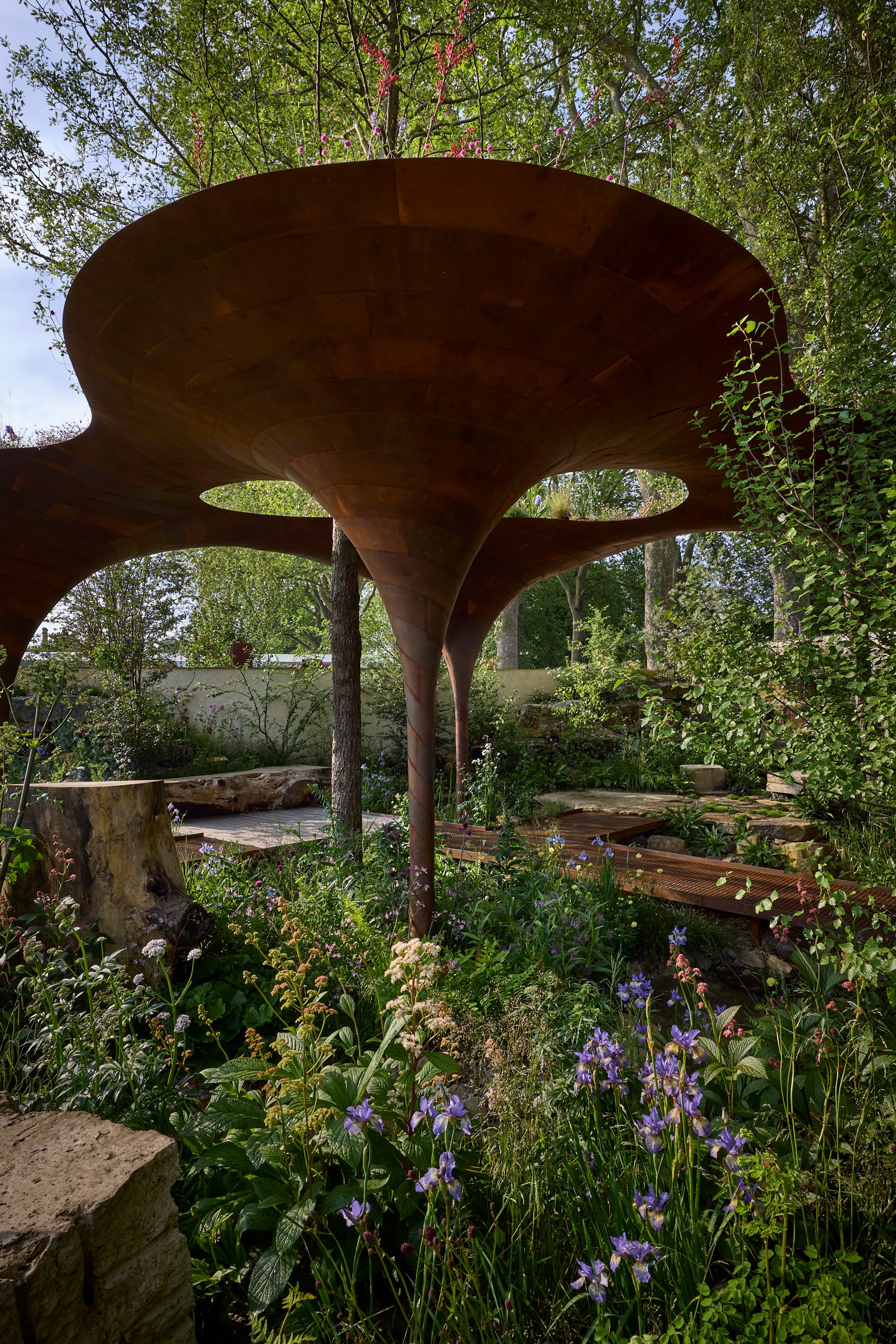 WaterAid 雨水收集綠建築 倫敦切爾西花卉展 RHS Chelsea Flower Show Je Ahn Tom Massey 雨水收集之簡便與挑戰:WaterAid花園的靈感與設計
雨水收集乃優質水源供應中最簡便的形式之一,然而,如何有效儲存卻經常成為挑戰。WaterAid利用一系列簡單且可負擔的雨水收集方法,將必需的水資源帶入容易缺水或水源受污染的地區,尤其是家庭與學校。屋頂收集法意味著水源可以在家附近取得,女性和女孩們無需花費數小時步行取水。此技術啟發了Je和Tom為WaterAid花園設計的結構,該結構旨在最大化收集和儲存雨水的表面積。
WaterAid的創新方法,使得每一滴雨水都成為寶貴資源,不僅減輕了日常生活中的負擔,更是讓社區在面對水資源匱乏時,擁有了應對的策略。Je和Tom的設計,不僅展示了雨水收集的技術,更展現了在自然界中尋找解決之道的智慧。這種設計的背後,蘊含著對環境的敬畏與對人類生活質量提升的追求,讓人們在花園中體會到大自然與人類共生共榮的美好圖景。