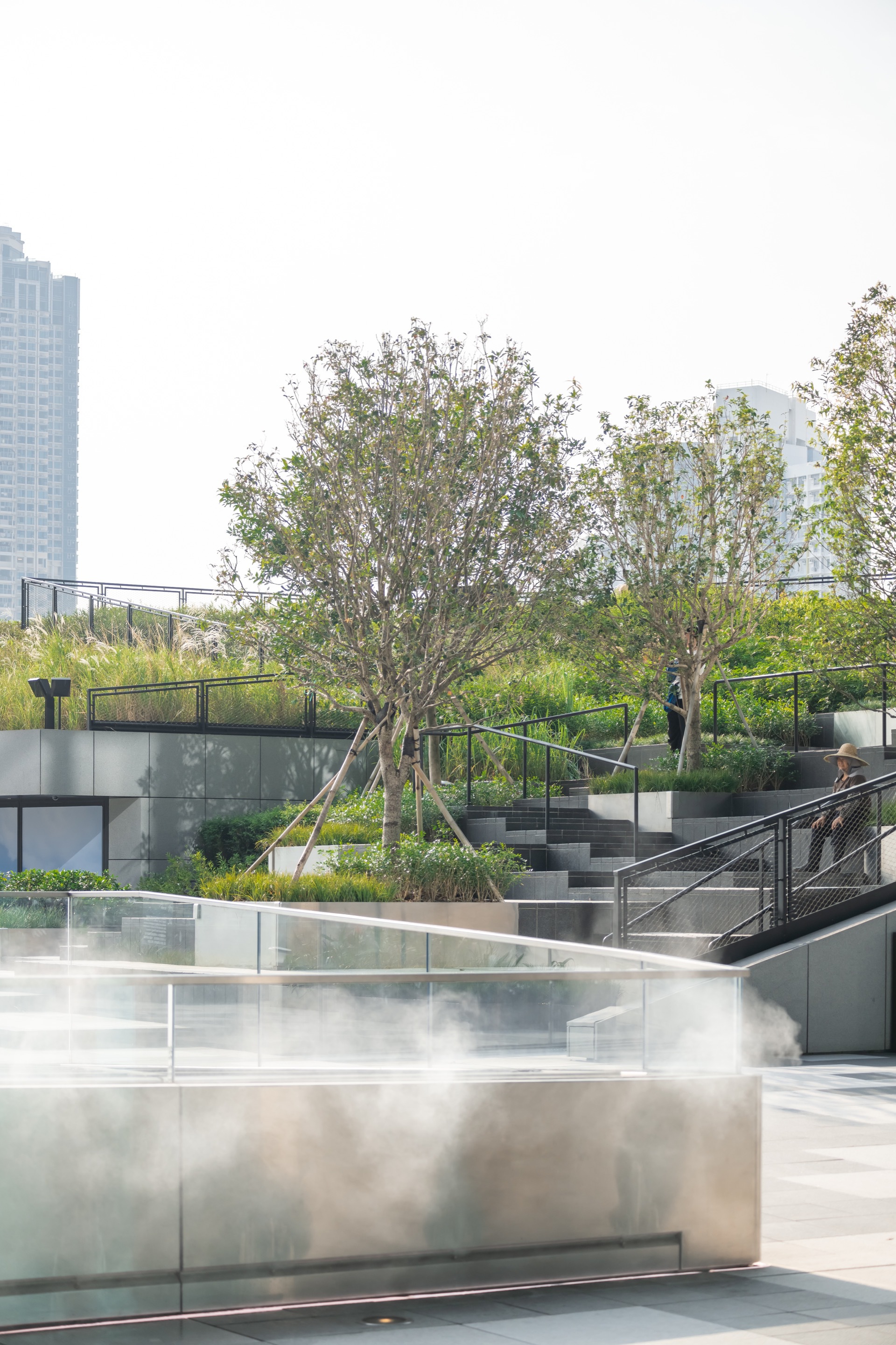 香港啟德機場AIRSIDE綜合地標大樓/Snohetta 在AIRSIDE的心臟地帶,一層層綠意盎然的梯田環繞著水霧飄渺的休憩區,為都市中的人們提供了一處獨特的休閒空間。這裡的設計展現了Snøhetta亞洲對環境與建築和諧共生理念的深刻詮釋。高聳的樹木與周圍的摩天大樓形成鮮明對比,強調了自然與人工結構之間的平衡。人們在這裡步行或靜坐,享受片刻的寧靜,藉由這樣的綠色空間,AIRSIDE不只重塑了香港的都市景觀,也為城市生活賦予了新的活力與節奏。