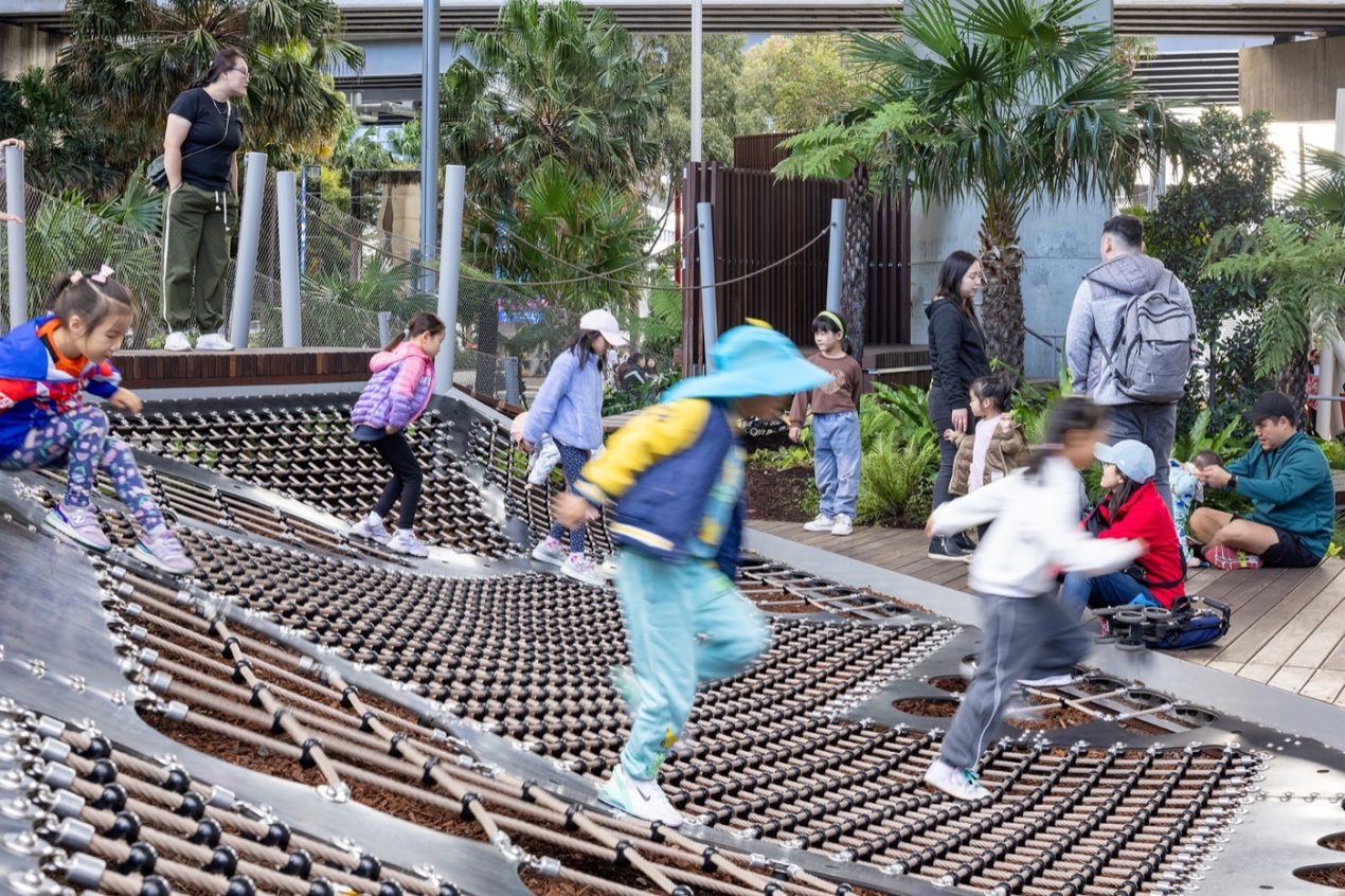 Darling Harbour Playground 雪梨達令港兒童遊戲場 溜滑梯 景觀設計 Aspect Studios 達令港遊樂場的網狀設施結合了趣味性與挑戰性,激發孩子們的運動與探索熱情。這樣的設計不僅鼓勵體能活動,還能增強孩子們的平衡感與協作能力。周圍植栽與開放空間營造出舒適的氛圍,讓家庭成員能一同享受戶外活動的樂趣。這裡已成為雪梨家庭聚會的熱門地點