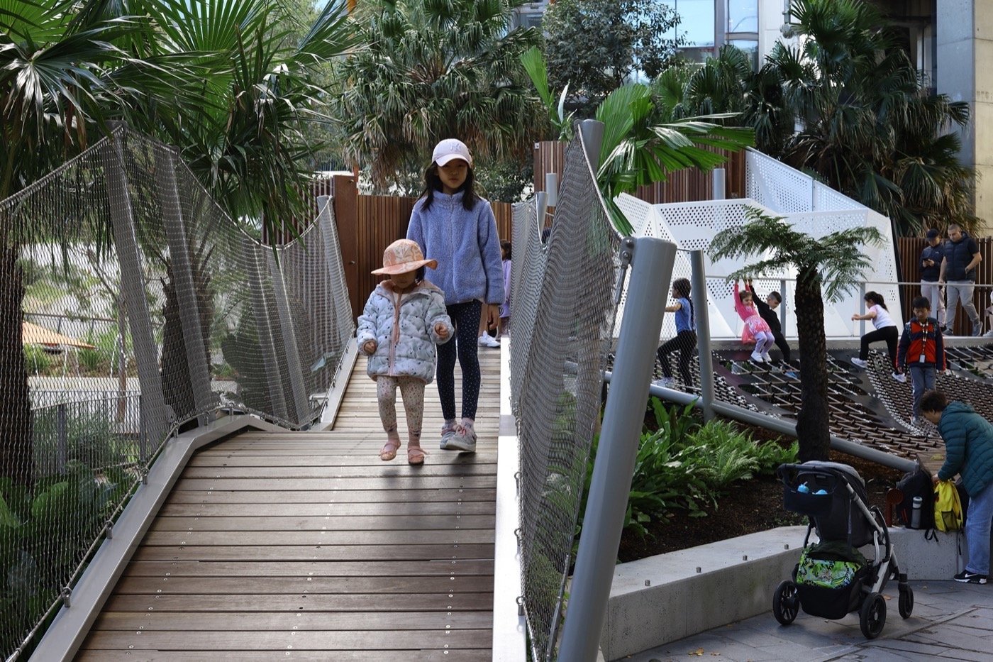 Darling Harbour Playground 雪梨達令港兒童遊戲場 溜滑梯 景觀設計 Aspect Studios 步行橋不僅為孩子提供探索的樂趣，也保障其安全。周邊綠植與現代化結構共同營造出自然與都市融合的氛圍，讓家長與孩子都能在這裡享受悠閒又互動的親子時光。這裡是培養孩子感官探索與冒險精神的理想場域