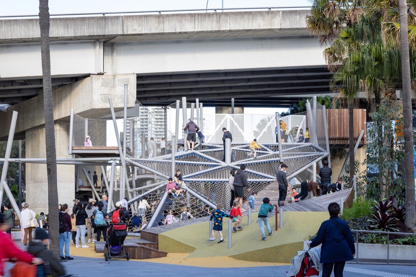 Darling Harbour Playground 雪梨達令港兒童遊戲場 溜滑梯 景觀設計 Aspect Studios  設計團隊以海洋風為意象，運用交錯的鋼構支柱及網索系統，創造出波浪起伏的遊戲平台，搭配蜿蜒的木製步道及黃色地坪，形成層次分明的活動場域