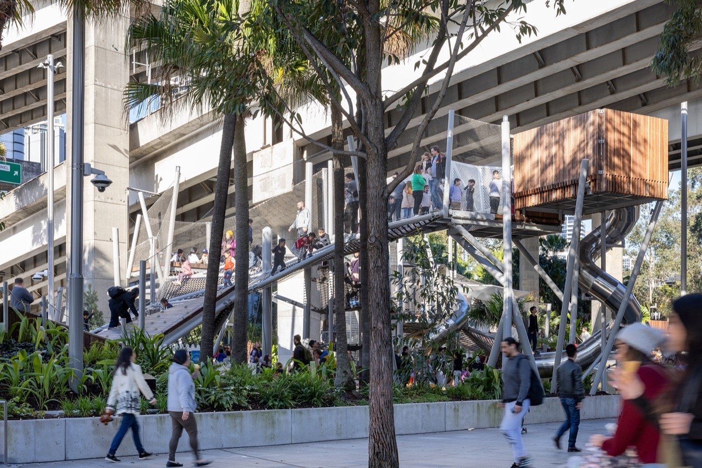 Darling Harbour Playground 雪梨達令港兒童遊戲場 溜滑梯 景觀設計 Aspect Studios  達令港新建遊戲場以創新設計手法詮釋海洋風情，引入不鏽鋼滑梯、攀爬架等遊具，搭配波浪造型木格柵及金屬網格設施，營造出兼具趣味及挑戰性的立體遊戲空間。遊戲場巧妙利用西部快速道路高架橋下方空間，不僅提供遮蔭，更化身為充滿活力的親子休閒場域