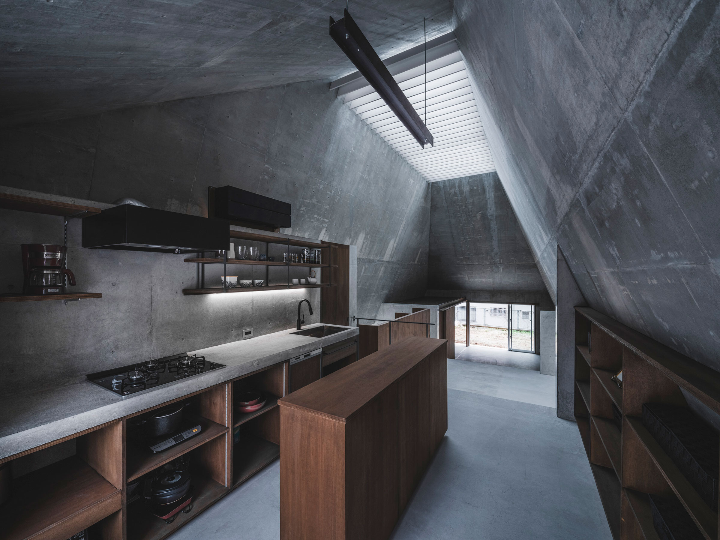 金字塔小屋內部廚房區域以清水混凝土與木材結合,展現簡約材質對比。定制的木製櫥櫃搭配鋼製開放架構,提供實用且美觀的收納功能。水槽區採用混凝土檯面與黑色水龍頭,延續空間的粗獷質感,無多餘裝飾,專注於材質本身的特性。屋頂斜面引導自然光線入室,增添層次感,使廚房功能性與美學兼具
