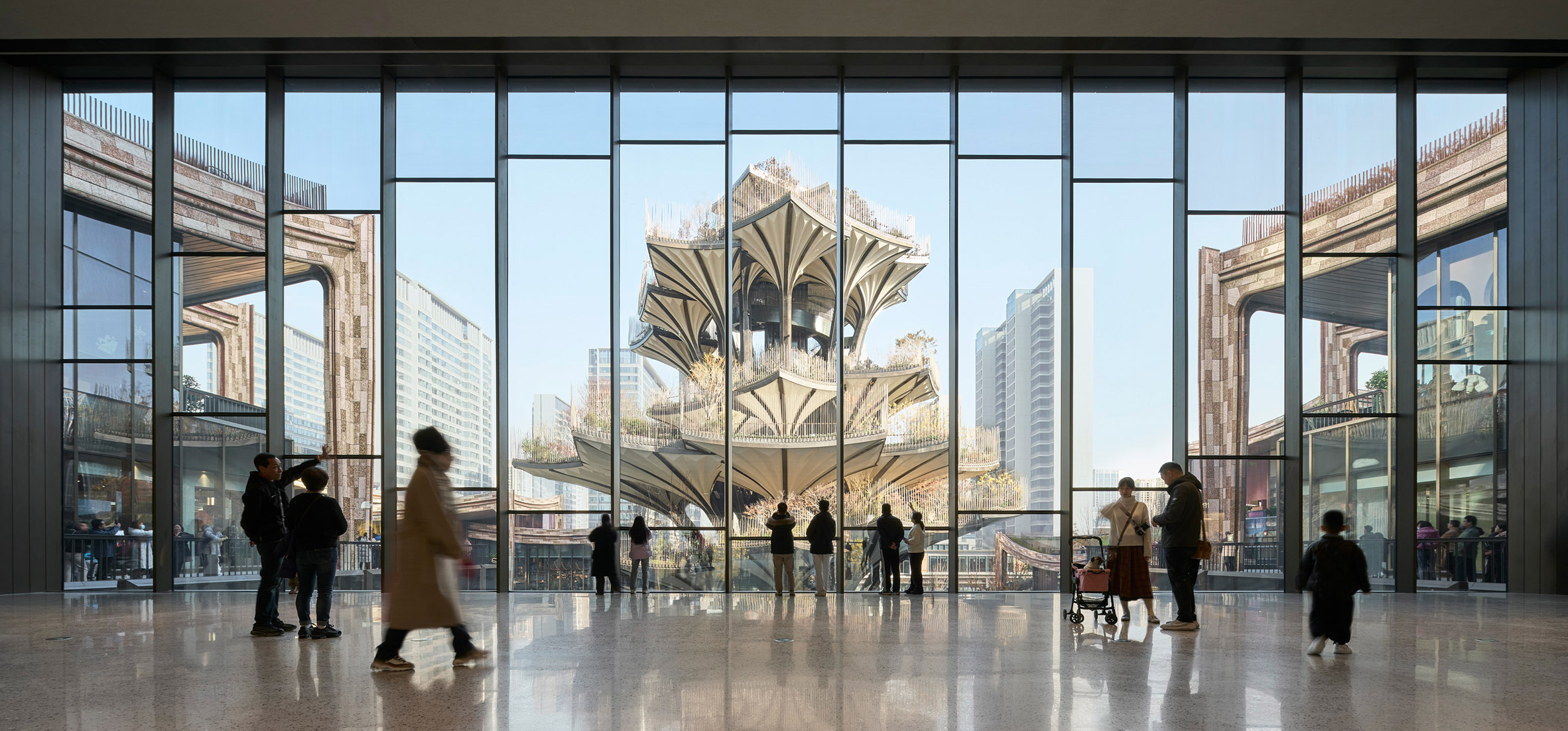 透過挑高空間外牆安裝的玻璃帷幕牆，人們可遠眺「西安樹」，那層層平台宛如立體花園向上攀升，Heatherwick Studio在室內設計的地坪使用研磨石材搭配金屬邊飾，增添視覺對比；拱形天花猶如波浪，與戶外拱門立面彼此呼應
