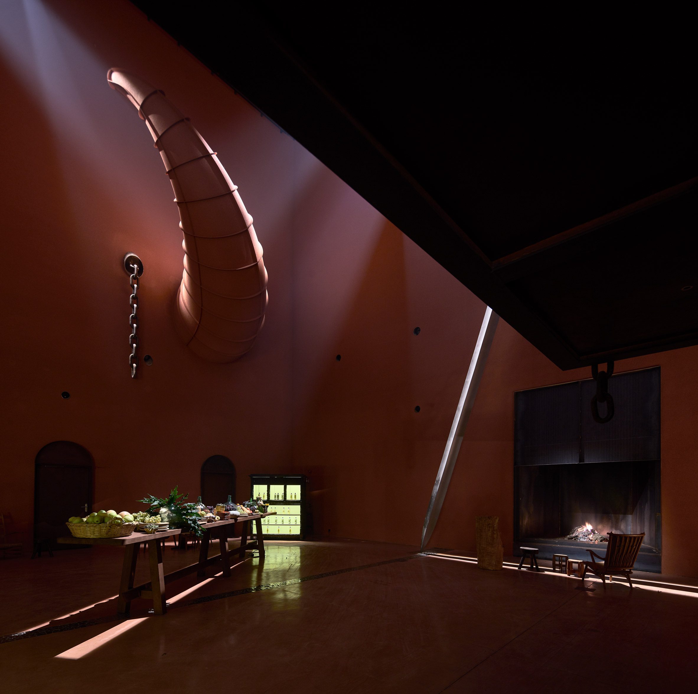 在壁爐旁的小型休憩區，一把巨大的鬥牛劍斜倚在牆上，與外部空間的牛角、半橄欖造型相互呼應。抬頭仰望，整片天花板覆蓋著大型壁畫，這些壁畫讓室內空間有著更豐富的視覺感受