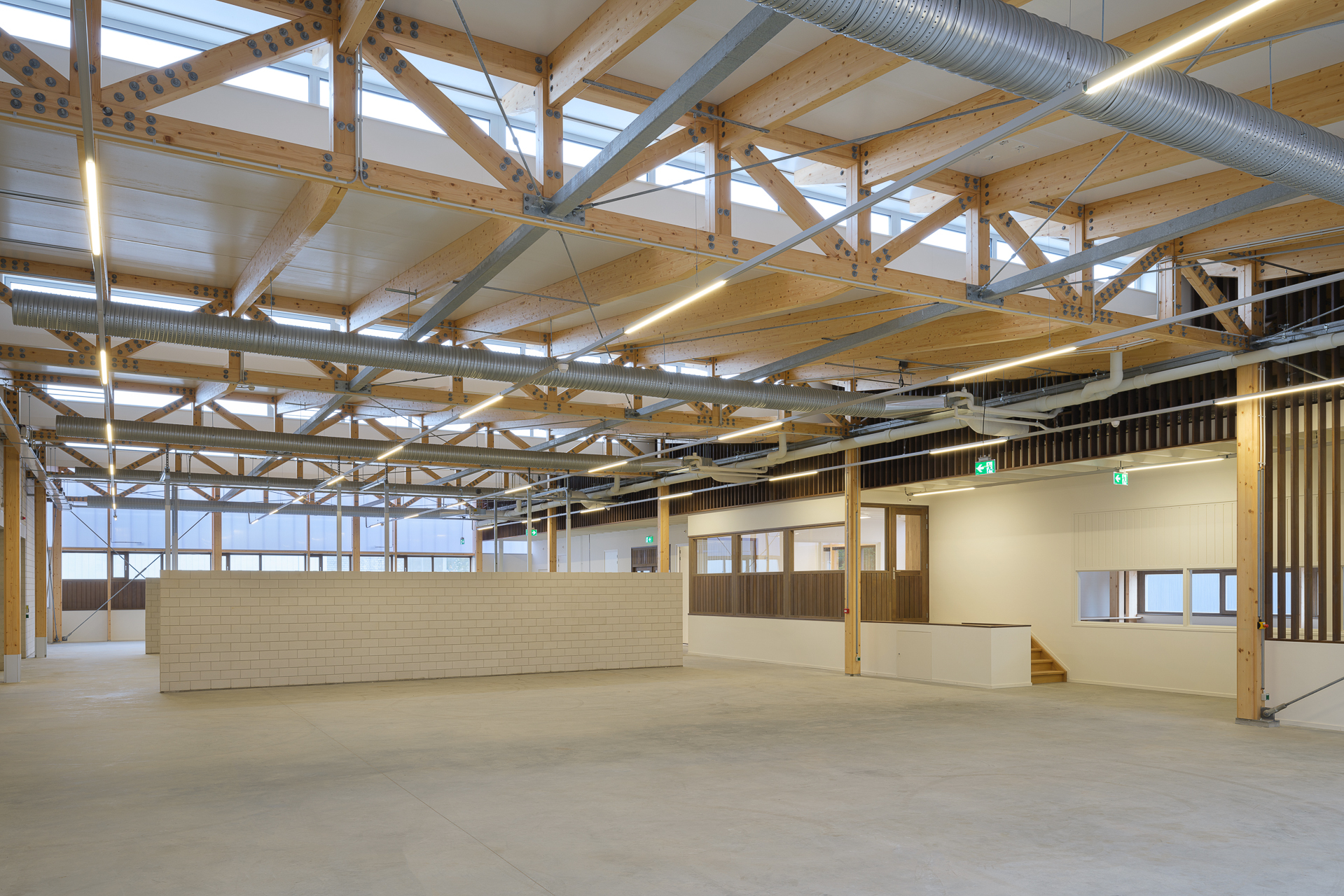 室內空間以木桁架結構和大量自然採光為主軸，樑柱與鋼件結合形成穩固的視覺張力。中央白磚隔牆劃分功能區域，柔和地融入開放式場域。開放式的金屬管道與天花板佈線設計呈現工業簡約美感，實現靈活使用的空間配置需求