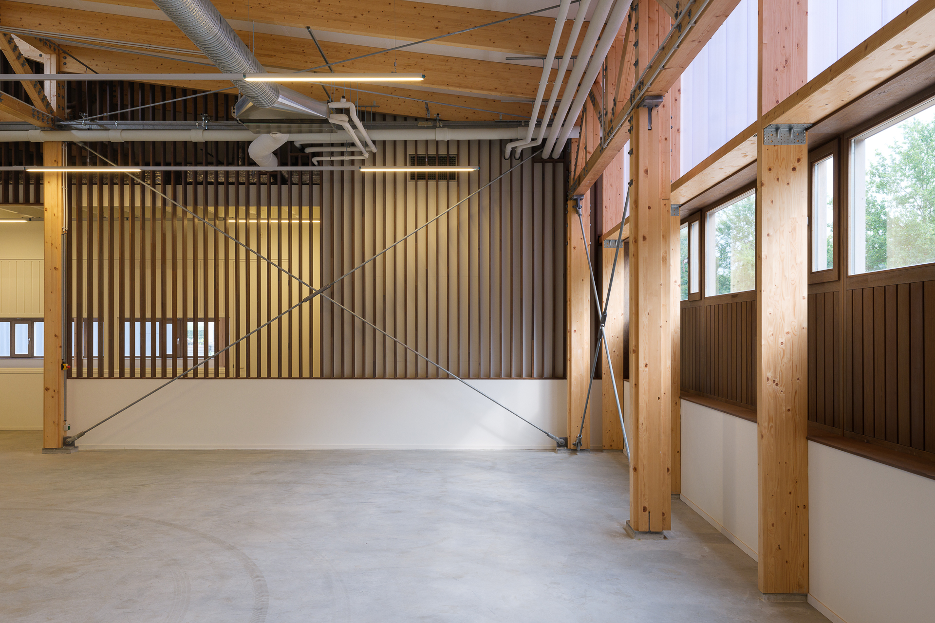 室內木構樑柱與垂直百葉式牆板規劃，劃出輕盈且通透的工作空間<
明亮窗帶與聚碳酸酯表面，柔和日光與外界視線，鋼構件強化結構並延伸視覺層次。EPOXY混凝土地坪簡化維護，同時兼顧耐用機能