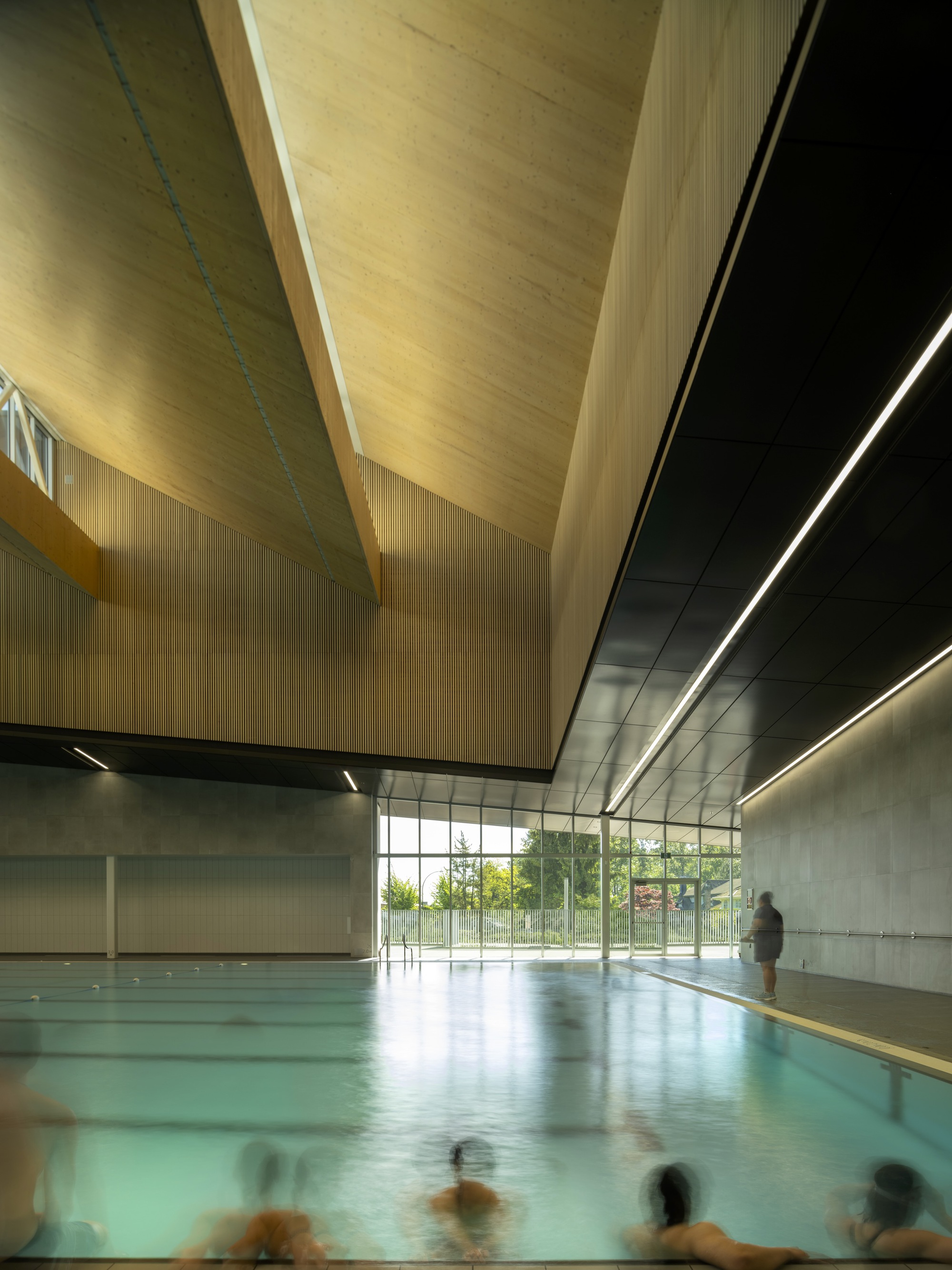 加拿大təməsew̓txʷ水上運動中心暨社區中心 運動館 體育館 təməsew̓txʷ泳池區以高挑木質天花板及折板設計創造溫馨氛圍,柔和的自然光透過玻璃牆流入,提升使用者舒適感。池區空間寬敞,地面防滑材質確保安全。泳池周圍的設計考量視線開放,連接室內外景觀,為使用者提供沉靜且宜人的水上運動場域