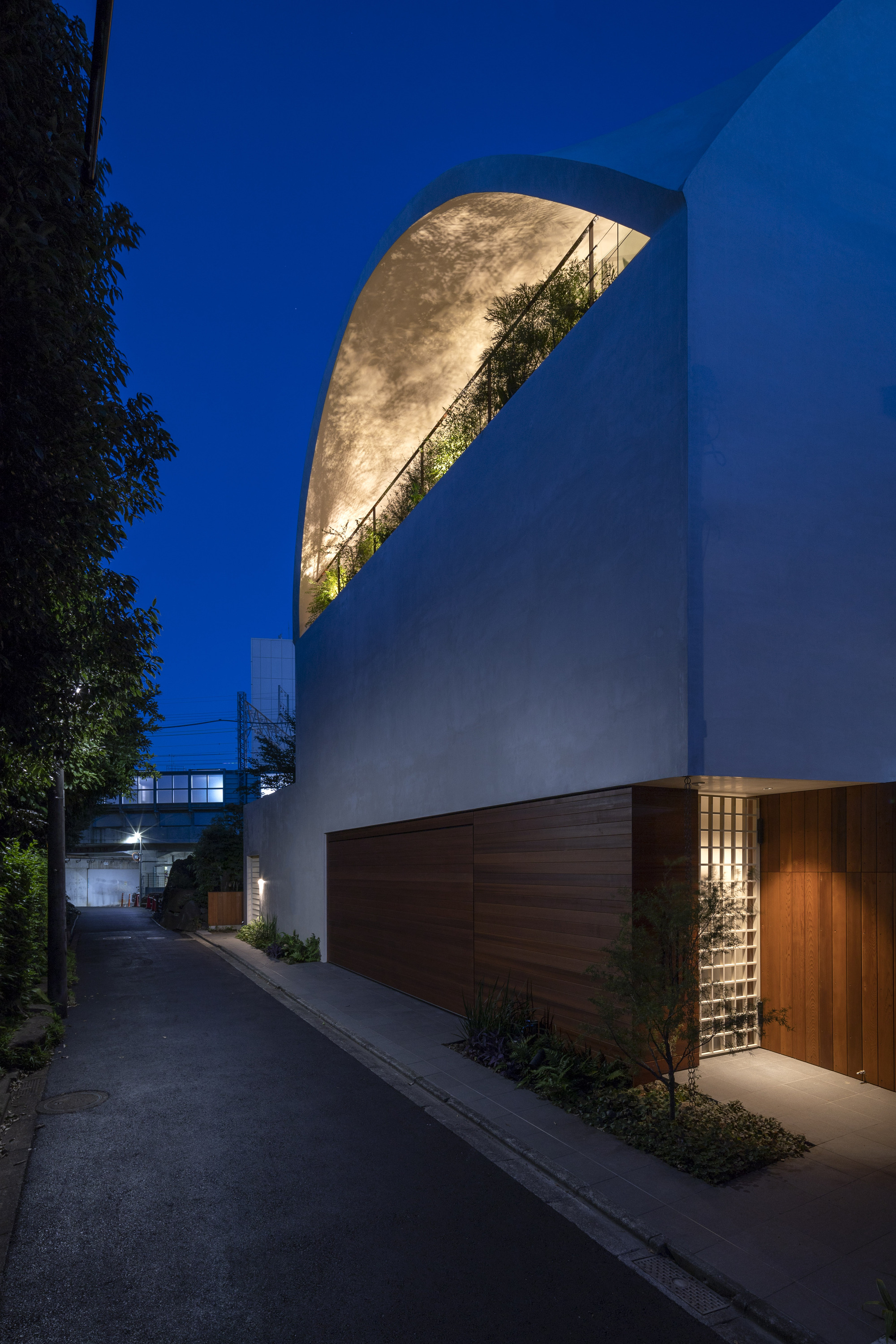 井川充司 天空洞穴 SKY CAVE 東京住宅 在燈光映襯下美麗浮現的建築外觀,猶如一座地區的地標。背景可見鐵路,弧形設計不僅包容了空間,也同時作為降低噪音的方式