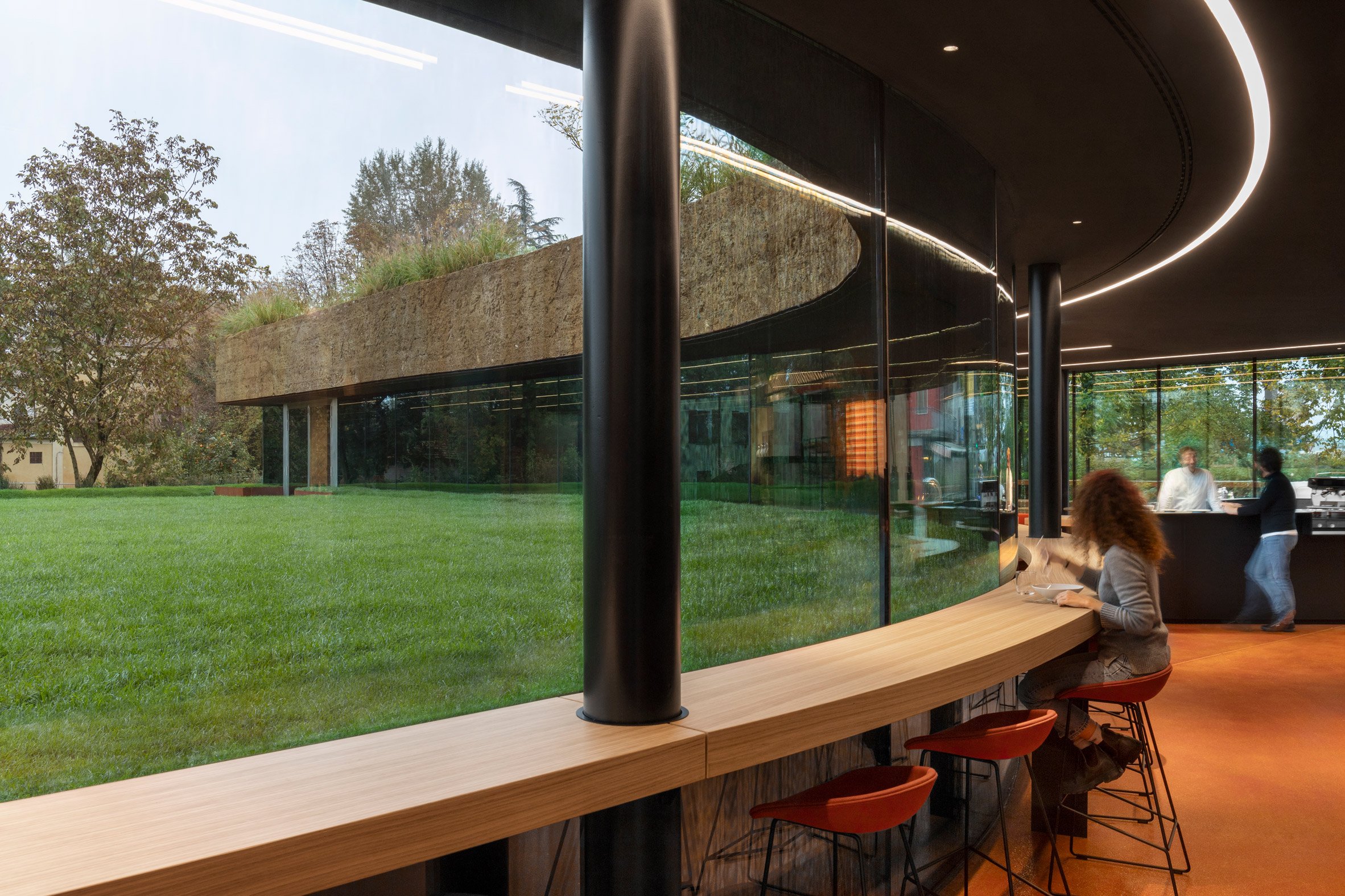 義大利餐廳 Carlo Ratti Associati Mutti restaurant 為了突顯屋頂的量體感,餐廳的室內設計特意將室內的牆面與天花板都採用了深色系的塗裝。而在材料的選擇上,也延續了 CRA 一貫的永續設計理念。餐廳內使用了百分之百可回收的材料,其中最受矚目的是那有著搶眼色彩的紅色地板,它是由樹脂混合回收的蕃茄皮製成的