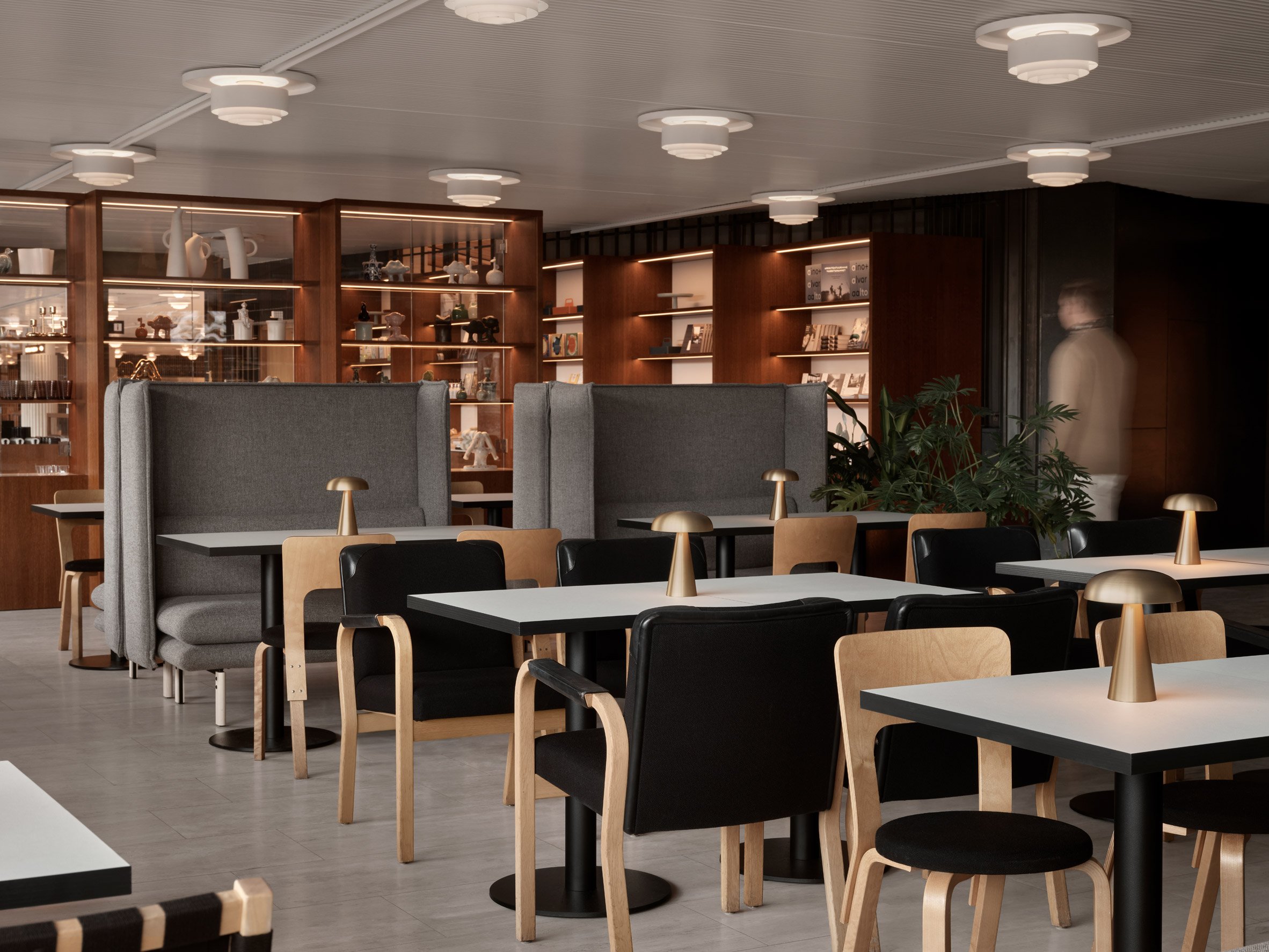 Finlandia Bistro餐廳:灰色高背座位與木質展示櫃相互呼應,櫃中擺放的器皿增添藝術質感。Artek木椅搭配黑色坐墊,營造輕鬆視覺效果。金屬檯燈散發柔和光暈,讓整個空間顯得舒適溫馨