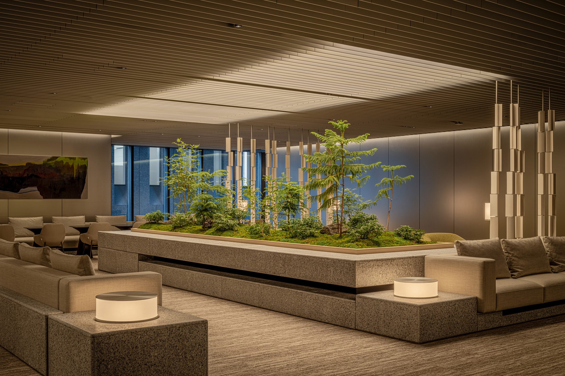 位於東京京橋博物館塔的接待大廳,中心以花崗岩打造的植栽區搭配自然植被,展現都市綠洲氛圍。柔和光線與天花格柵相呼應,帶來層次感與舒適感,灰米色沙發及燈具為 Cassina 的作品,散發高雅而平靜的質感