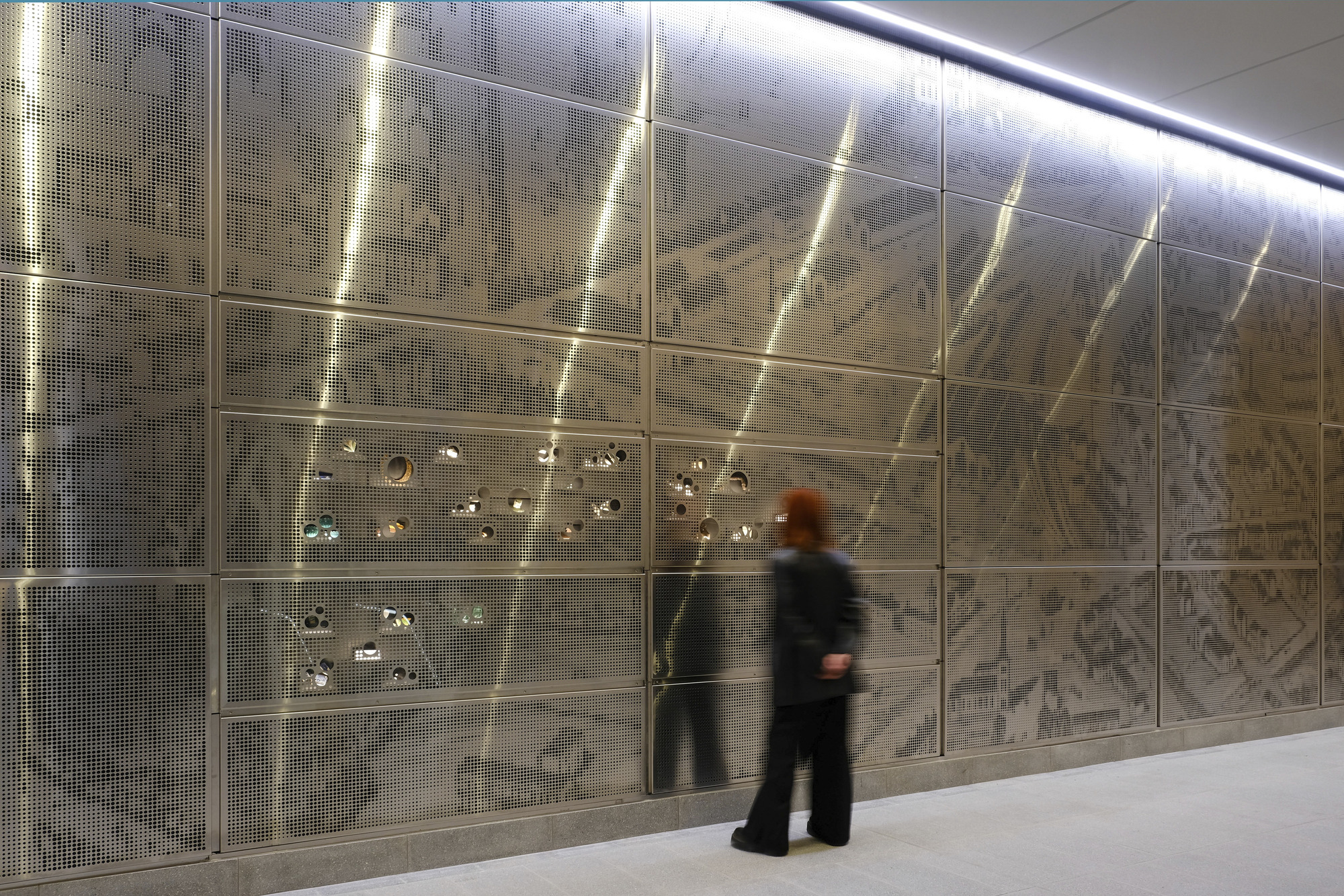 雪梨中央車站 Sydney Central Station Renovation Woods Bagot 裝飾牆以金屬沖孔板為材質，展現城市歷史地圖的抽象紋理，結合內嵌的光影效果，營造出動態視覺。燈光細緻地突顯板面細節，為通道增添藝術氛圍