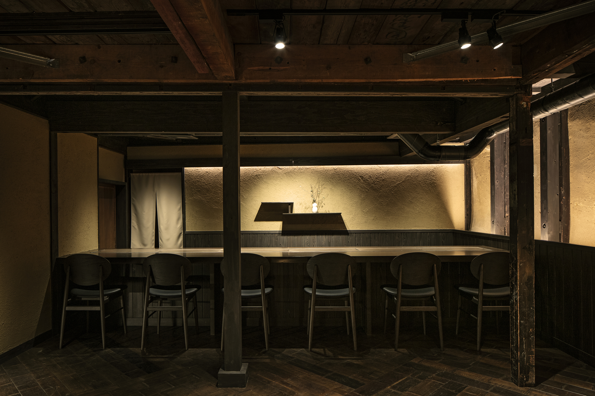 Nazuna Kyoto Higashihonganji 京都 旅館 東本願寺 STUDIO ALUC 低調燈光襯托土壁肌理,木作吧檯與黑色曲木椅排列其間,牆上留白僅以枝影點綴,營造出靜謐沈穩的用餐氛圍