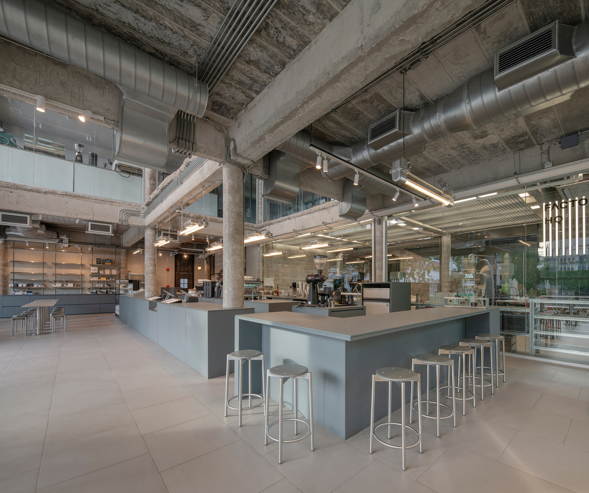 TasteSpace 室內設計 泰國曼谷冠軍咖啡店「Factory Coffee」 運用裸露管線與灰色調大型吧台，搭配金屬高腳椅烘托工業感，開闊區域讓咖啡製作流程更直觀，也提升顧客互動性