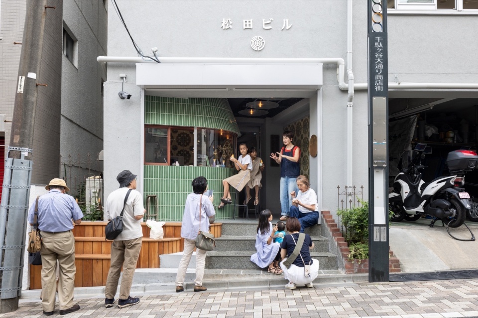 這棟大樓位於坡道上，其入口原本設有台階來化解高差，使得街道與建築之間存在一定距離。然而，隨著這家店舖的加入，台階不僅成為了人們休憩的長凳或放置物品的平台，還賦予了整個入口空間新的意義。這個小店不僅為建築入口和街道增添了生氣，也期待未來成為人們喜愛和依賴的一部分。