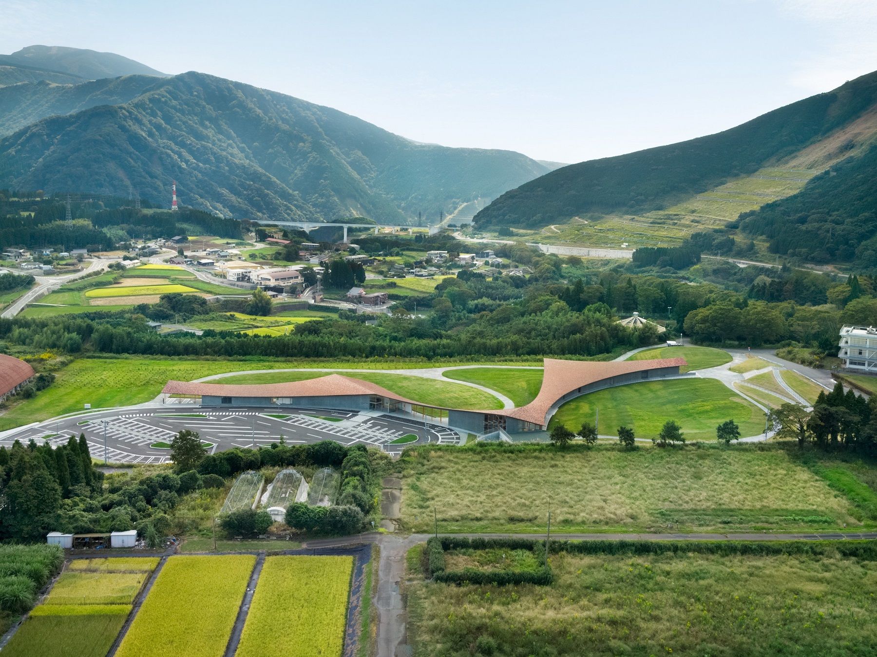 Kumamoto Earthquake Museum KIOKU熊本地震 震災ミュージアム KIOKU 設施座落於南阿蘇村（南阿蘇村）的舊東海大學阿蘇校園範圍內，此地點能格外強烈地感受到阿蘇地景的壯闊。考量到周圍環繞著舊一號館等震災遺構的特殊條件，設計避免將所有體驗侷限於建築內部。反之，透過一道尺度寬宏、呼應地景的巨大屋簷，創造出開放性的半戶外空間，鼓勵來訪者在此眺望周遭環境，以各自的方式感受、思考自然的巨大力量