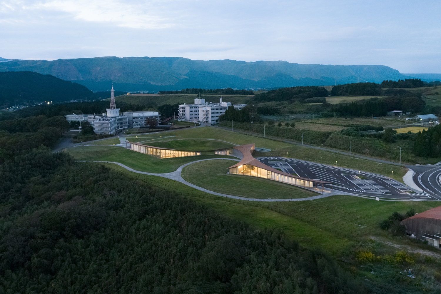 Kumamoto Earthquake Museum KIOKU熊本地震 震災ミュージアム KIOKU 博物館選址極具深意，緊鄰著舊東海大學阿蘇校舍1號館（旧東海大学阿蘇校舎1号館）。此棟建築在強震中承受嚴峻考驗，雖位於活動斷層正上方，卻奇蹟般未完全倒塌，連同地表破裂的斷層一同被保存下來，成為極其珍貴的震災遺構