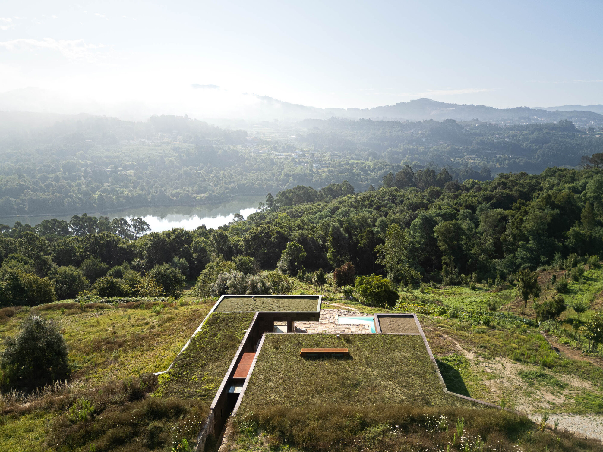 Casa da Levada 位於葡萄牙 Paredes 鄉間,背倚 Tâmega River ,建築如山巒自然延展的稜線般嵌入地形。由 Tsou Arquitectos 操刀,設計團隊捨棄與地景對抗的姿態,轉而擁抱基地原貌