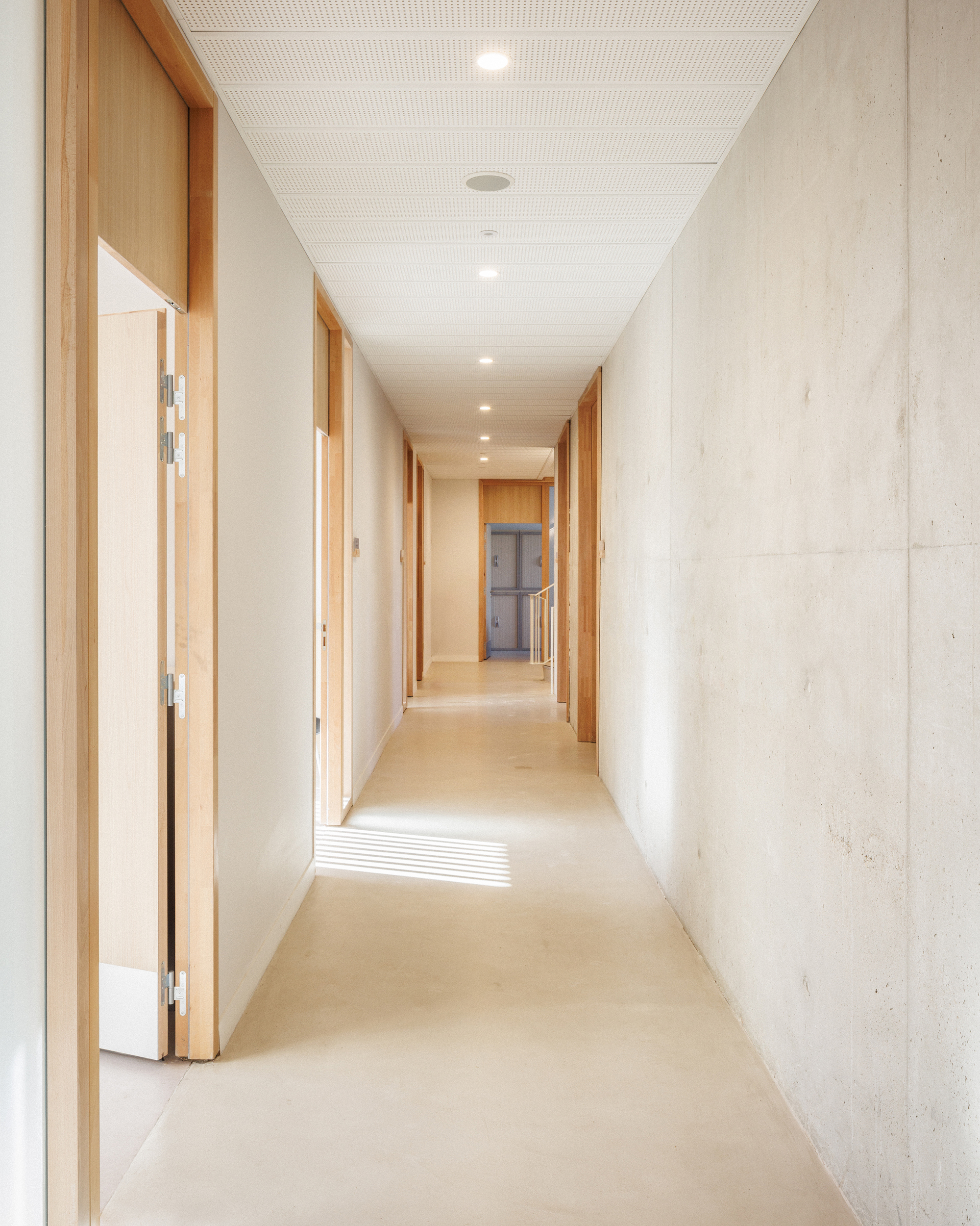法國警察局 Épernay Police Station Explorations Architecture 清水模牆面與木門框相映,警察局內部走廊展現簡約且明亮的空間語彙,強調功能效率與舒適工作的平衡