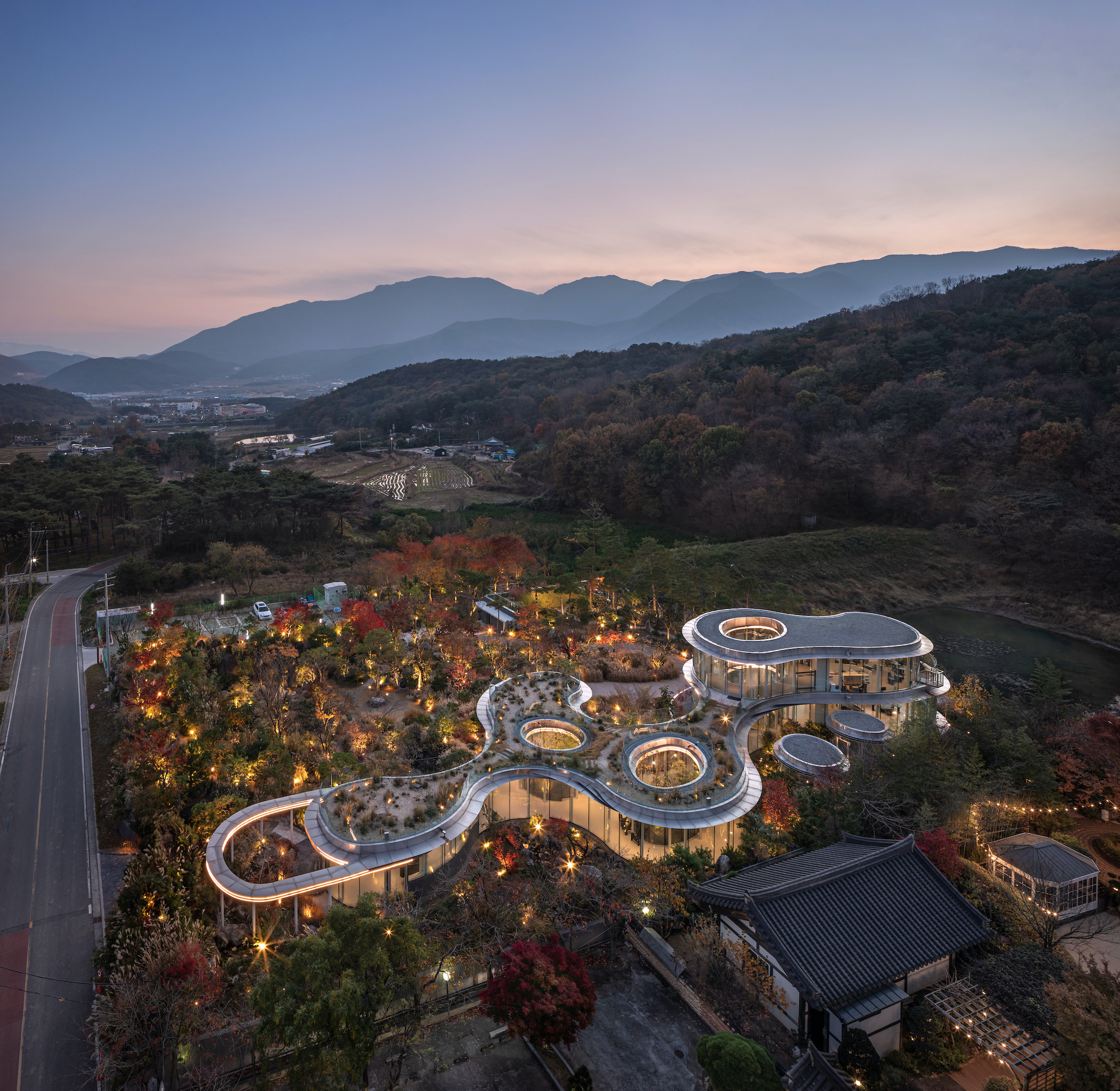 韓國複合文化空間蔚山市蔚州郡「MIGIUI」Architect-K 名稱「MIGIUI」（韓文「미지의」）直指設計核心——探索建築與自然間的模糊地帶。團隊刻意保留基地東側的施工痕跡，讓新舊地貌並置對話；夜間照明採用2700K色溫，模擬月光穿透樹梢的效果