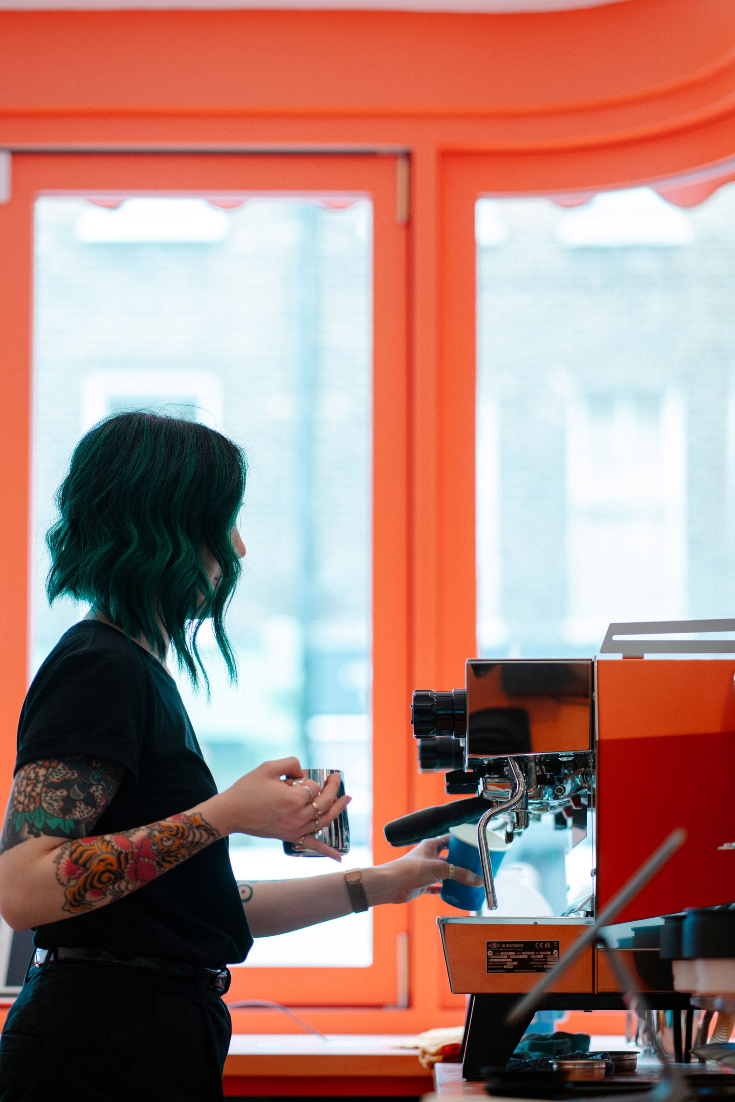 英國倫敦室內設計 Goodge  複合店Cona Tigg Coll 咖啡館吧檯以鮮亮的珊瑚橘色為主軸，明亮採光搭配義式咖啡機，提供顧客放鬆舒適的消費環境，呈現品牌青春活力的形象