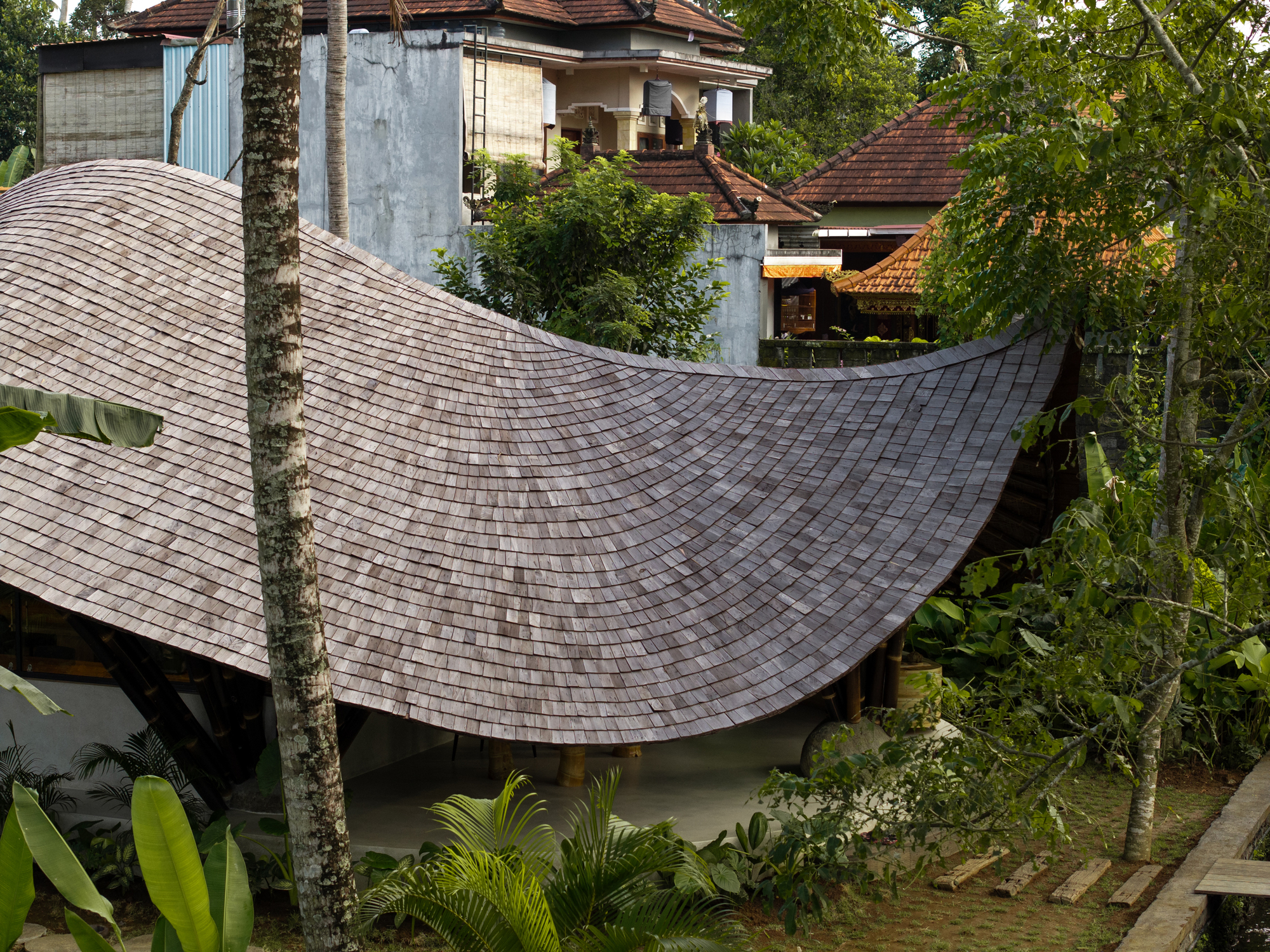 印尼度假勝地峇里島烏布 Ubud Bali 辦公室 竹構 bamboo structure Studio Lodtunduh Pablo Luna Studio Studio Lodtunduh 波浪狀屋頂由耐候的烏林木瓦片鋪成，隨著黑竹結構輕盈延伸，與烏布村落的熱帶植被及鄰近建築自然呼應