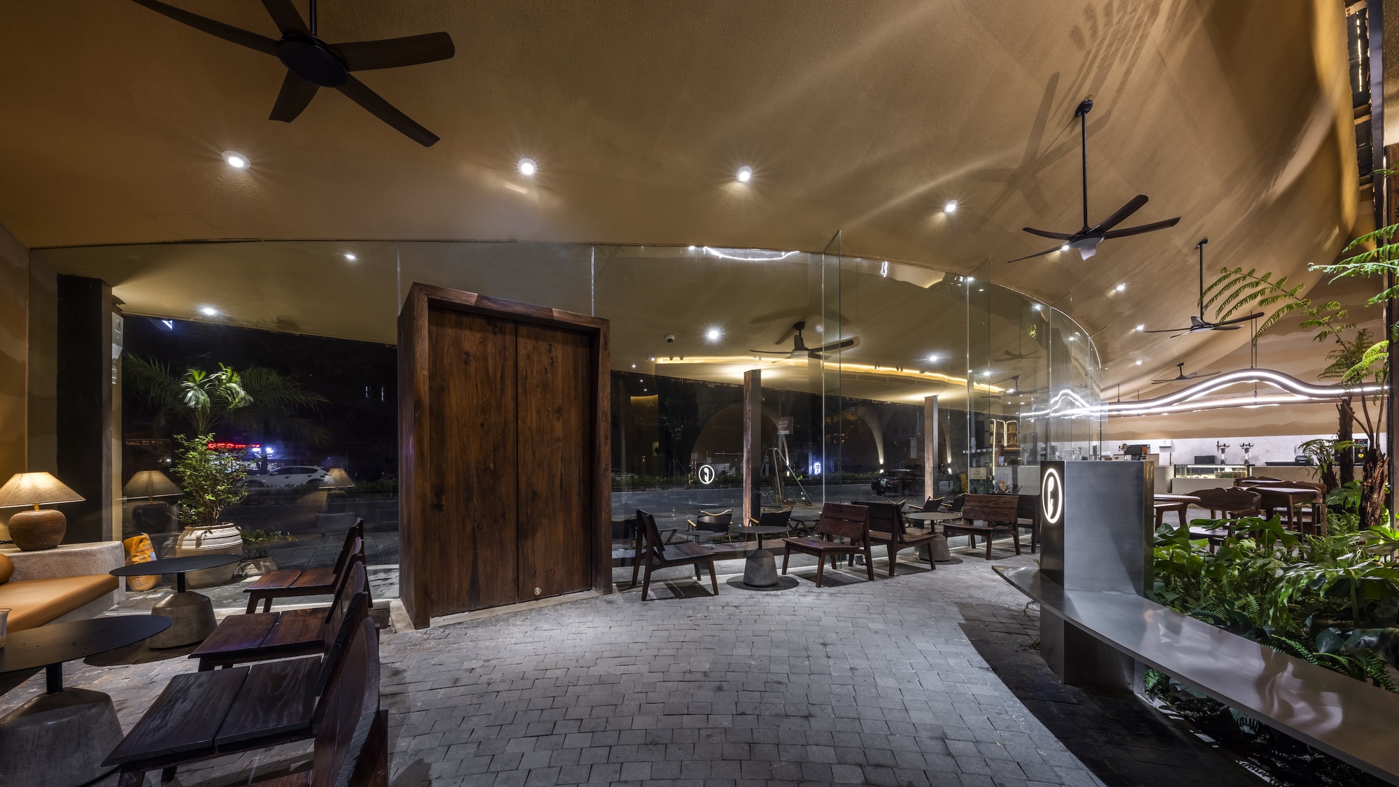 日光與陰影在牆面、木紋與植栽之間遊移，讓空間不只是靜止的場域，而是一段動態敘事的時間劇本。戶外座席環繞綠意與原始材質，使整體氛圍具備熱帶午后氣息，茶香氤氳時，光影輕拂牆面，記憶也開始在空間裡發酵