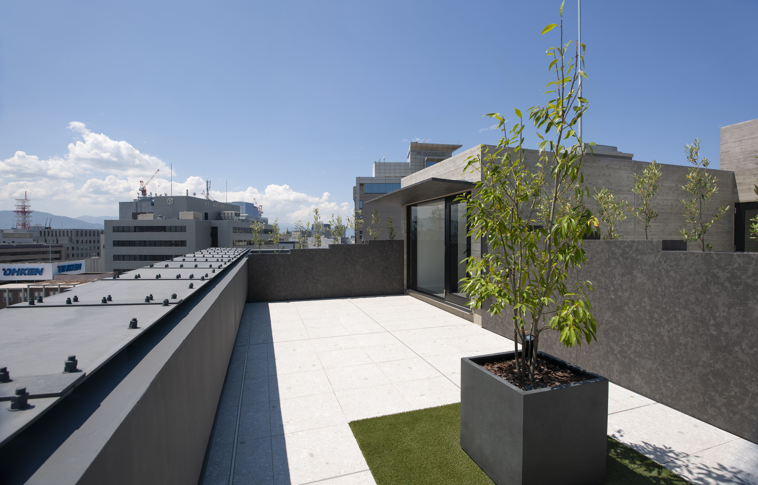 迫慶一郎 Keiichiro Sako SAKO建築設計工場 SAKO Architects 福岡 VECTORS in Fukuoka 辦公大樓 屋頂層透過清水模牆與植栽界定出靜謐邊界，石材鋪面延伸至城市遠景，構築開放轉折的收尾。高低錯落的綠意與建物量體呼應街廓高度，回應福岡都市密度與天際線節奏