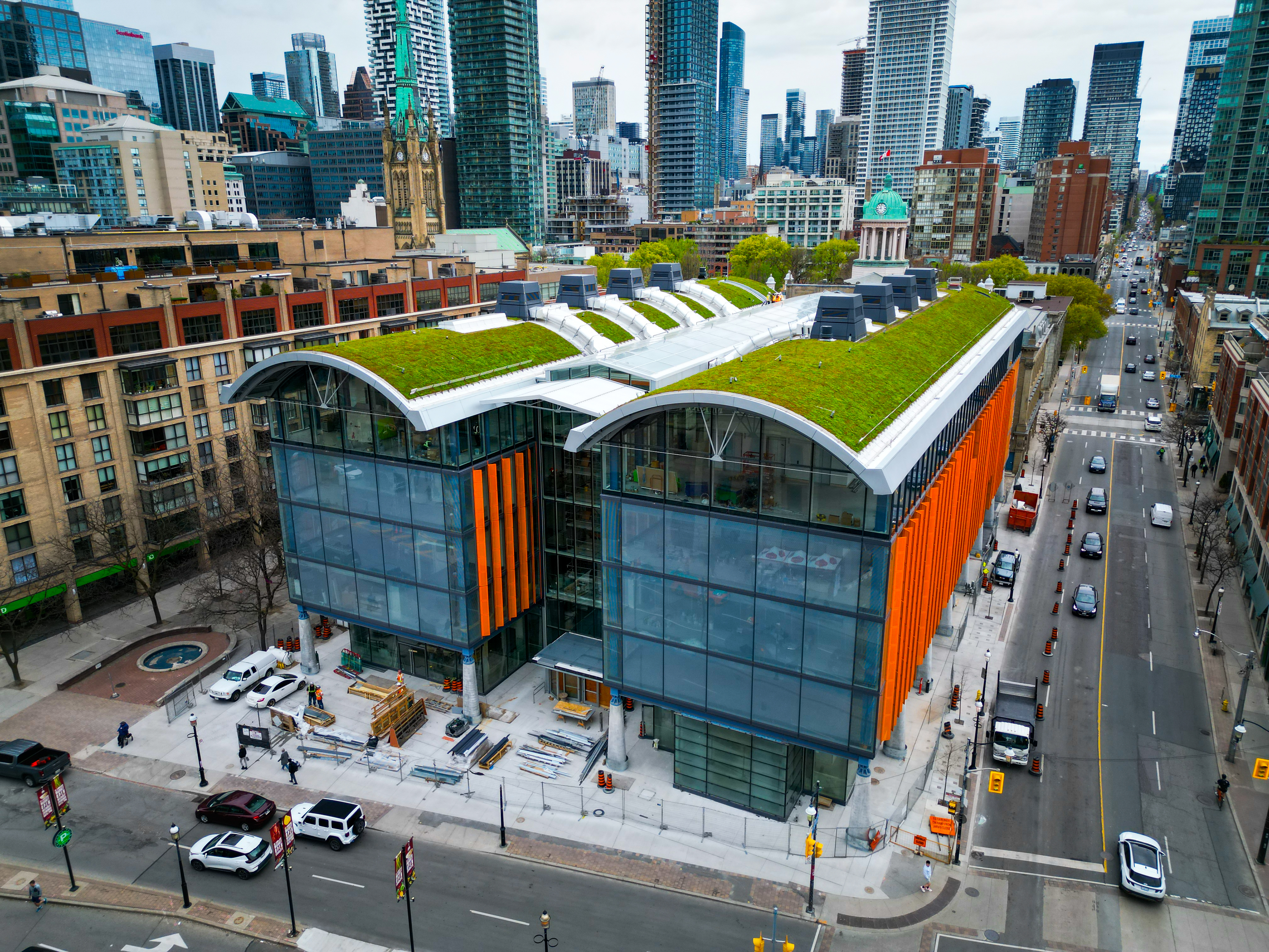 坐落於多倫多新舊建築交織的都市紋理中，聖羅倫斯市場北翼以其醒目的雙弧線綠色屋頂，確立了自身的座標。建築立面由大面積玻璃帷幕與序列性的橘紅垂直飾板構成，呈現通透的視覺感受，並與周遭的歷史街廓及現代高樓形成有趣的視覺對話