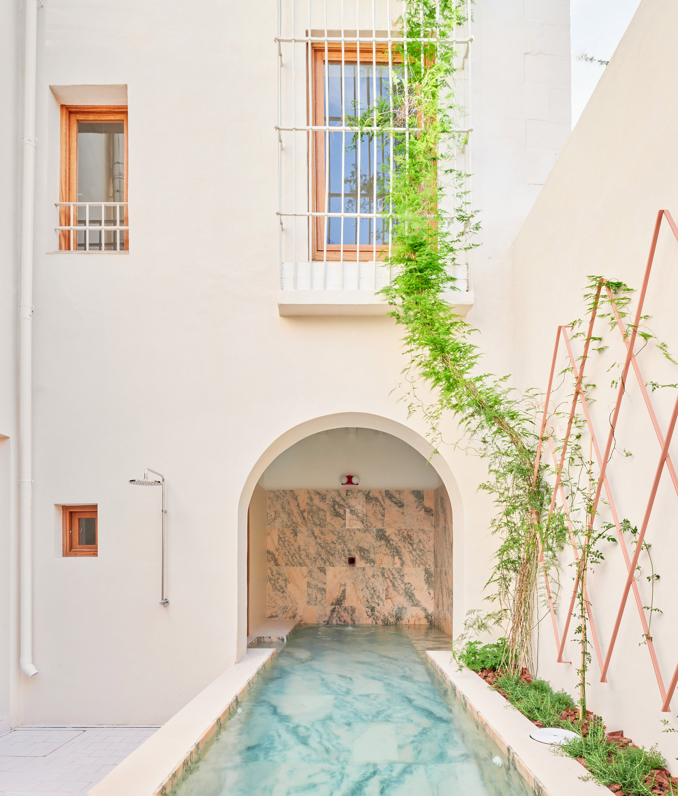 El Puerto de Santa María 住宅室內設計 Lucas y Hernández-Gil 西班牙 高牆圍繞的內院裡，狹長的碧綠水道是視覺焦點。水道盡頭，粉色大理石龕室與簡潔的戶外淋浴設備形成對話。銅色菱格網架，引導著綠意藤蔓攀附向上，為這方垂直的靜謐庭園，注入了奮力生長的生命氣息