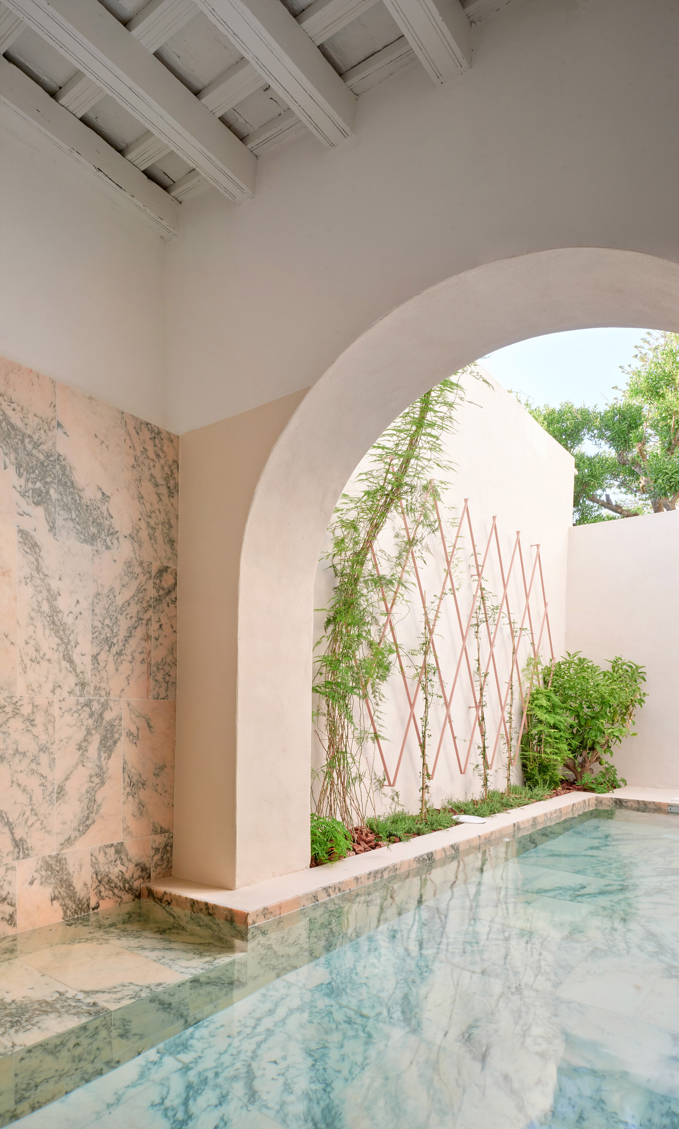 El Puerto de Santa María 住宅室內設計 Lucas y Hernández-Gil 西班牙 庭院的泳池是一處隱密的奢華空間。一道厚實拱門劃開室內與戶外，牆面鋪設了帶有灰色紋理的粉紅大理石，與池中碧綠水色相互輝映。牆上的銅色菱格攀爬架，讓藤蔓沿牆而上，在新舊交陳的氛圍中，圍塑出一片靜謐安詳的水上花園
