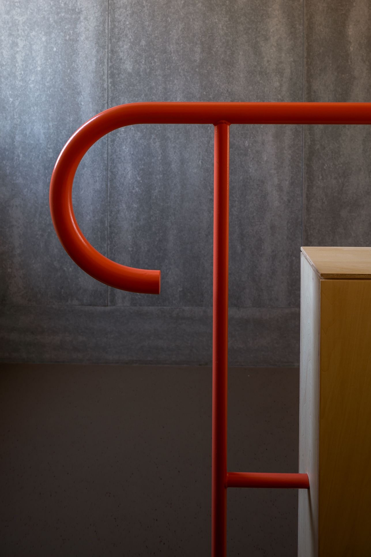 野口修 Sanmei 辦公室 樓梯扶手的細部設計，將建築外部的鋼骨語彙引入室內。管狀的鋼材彎折出簡潔的圓弧，並漆上與結構相同的鮮明紅色。在沉靜的深灰牆面與淺色木質家具旁，這抹紅色不僅是視覺焦點，也成為串連內外空間、引導使用者動線的鮮活線索
