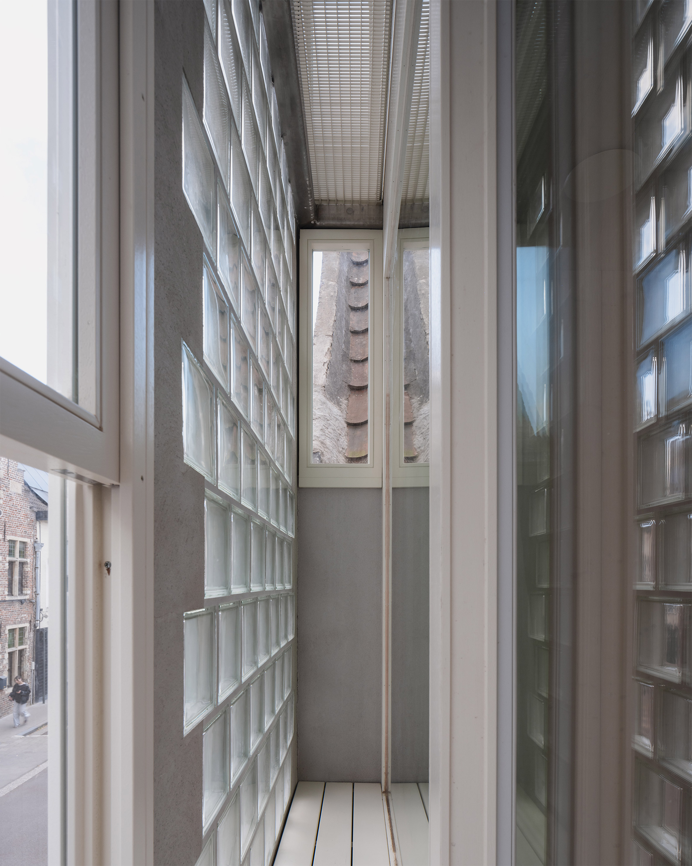 比利時 根特 Ghent 玻璃磚屋 Delmulle Delmulle Architecten Glass Brick House 玻璃磚立面特別採用了雙層皮層（double-skinned facade）的構造。外層是玻璃磚牆，內層則為高性能的全層高落地玻璃，兩者間的空氣層形成一道有效的隔熱緩衝區，並由金屬格柵地板界定出可供檢修的貓道