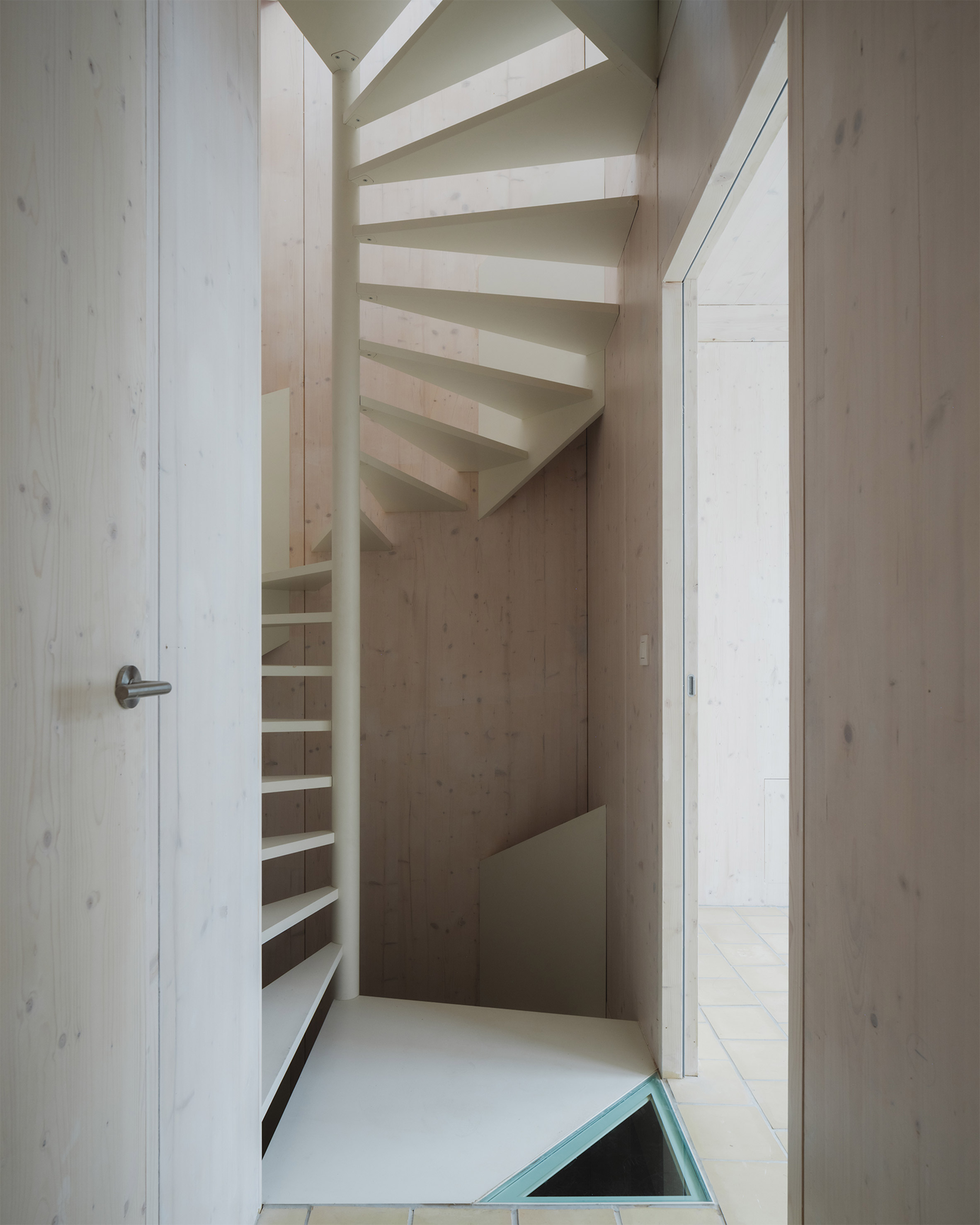 比利時 根特 Ghent 玻璃磚屋 Delmulle Delmulle Architecten Glass Brick House 金屬螺旋梯蜿蜒貫穿樓層核心，與CLT木牆構成明暗交錯的垂直動線。三角形玻璃天井為地下層引入微光，在極小腹地中拉出一條內向、靜默且精準的光線軸線