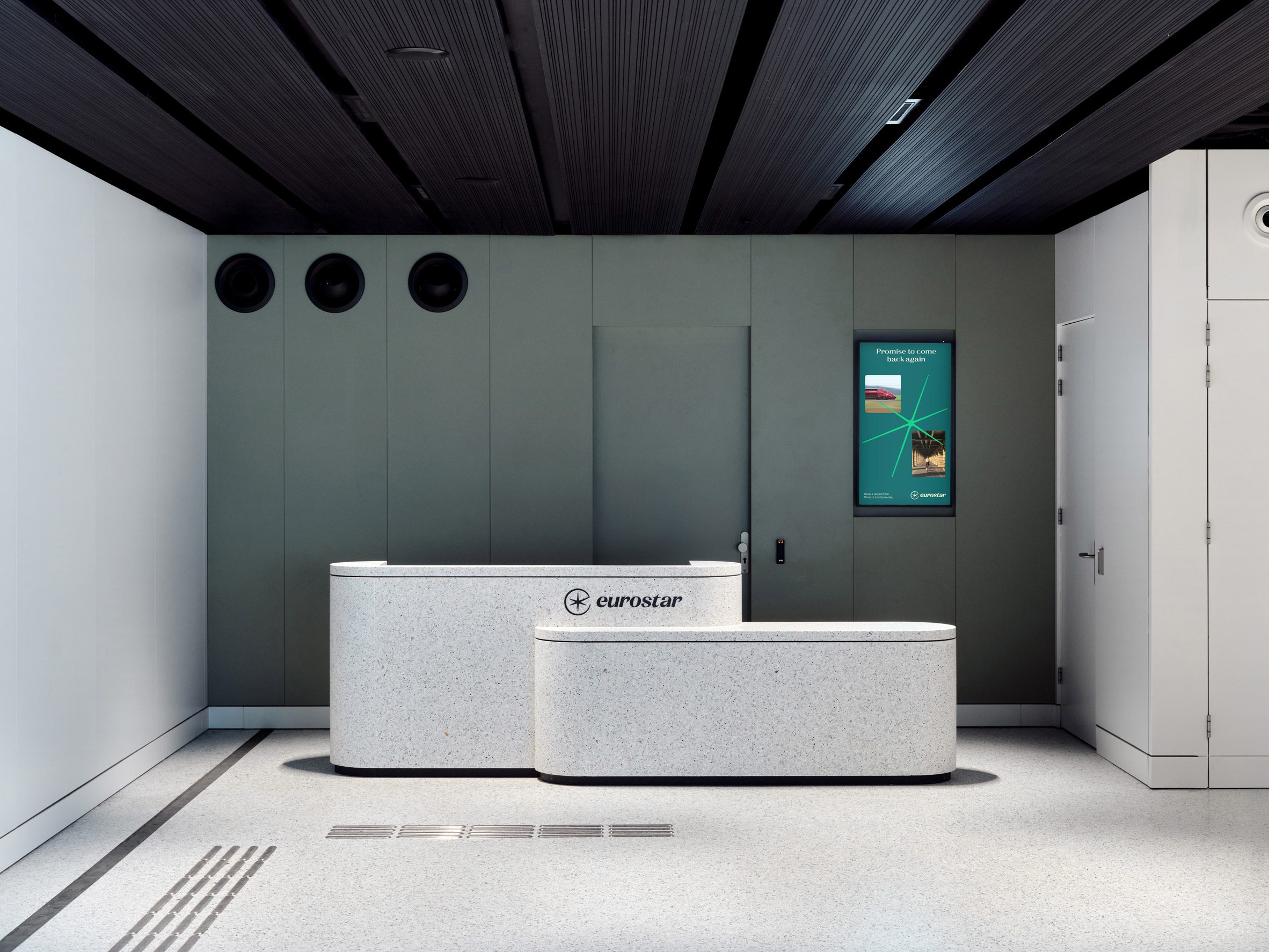 Superimpose Architecture 歐洲之星 Eurostar 候車室 阿姆斯特丹中央車站 Amsterdam Centraal Eurostar 英國航廈內的接待櫃台採用水磨石材質，出自 +Halle 與 InteriorWorks，與綠灰色牆面和黑色天花共同構築沉穩簡潔的迎賓空間