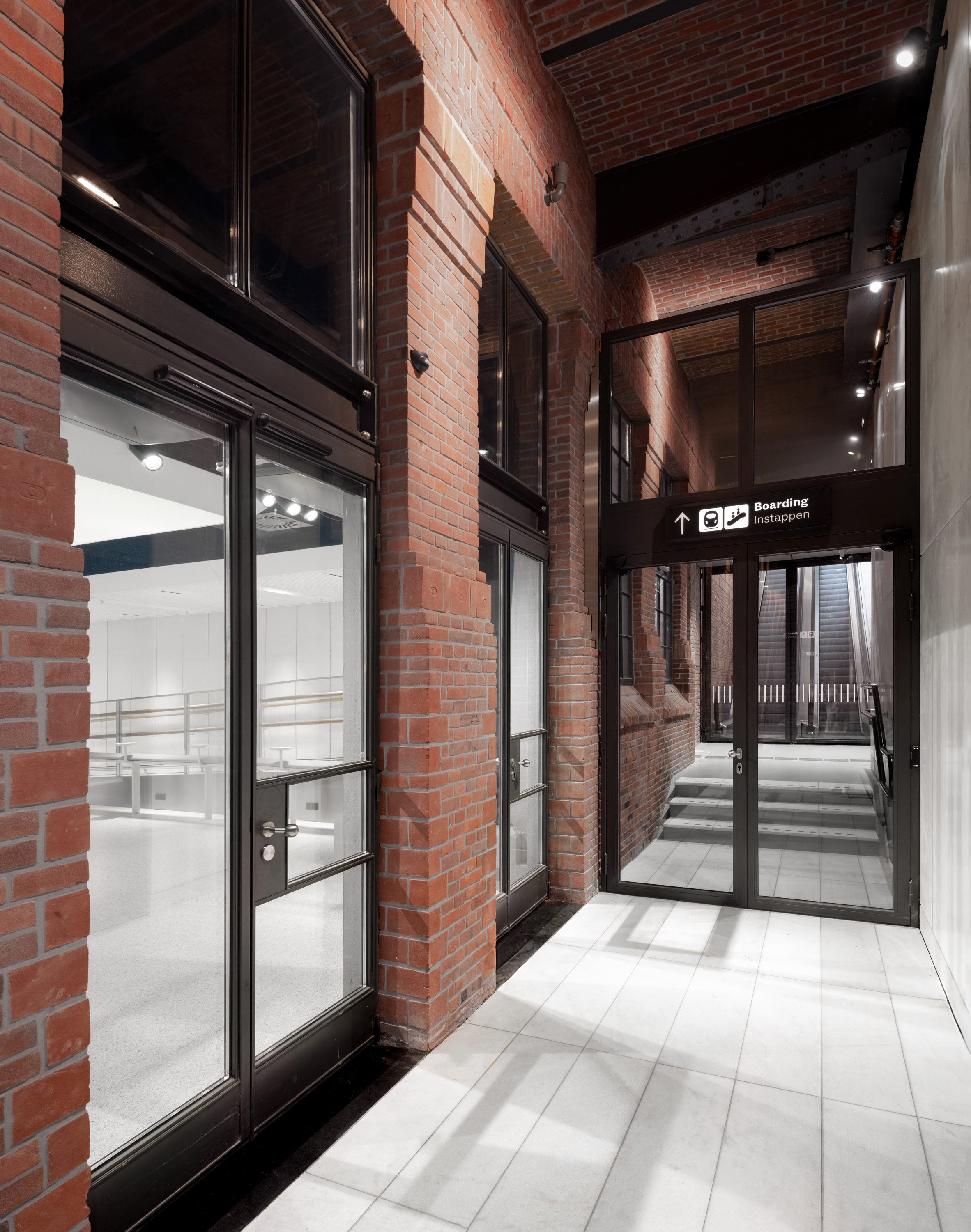 Superimpose Architecture 歐洲之星 Eurostar 候車室 阿姆斯特丹中央車站 Amsterdam Centraal 紅磚拱廊與鋼構天花交錯，導引旅客通往登車方向；光影映照在石板地面，喚醒十九世紀車站建築的節奏與層次