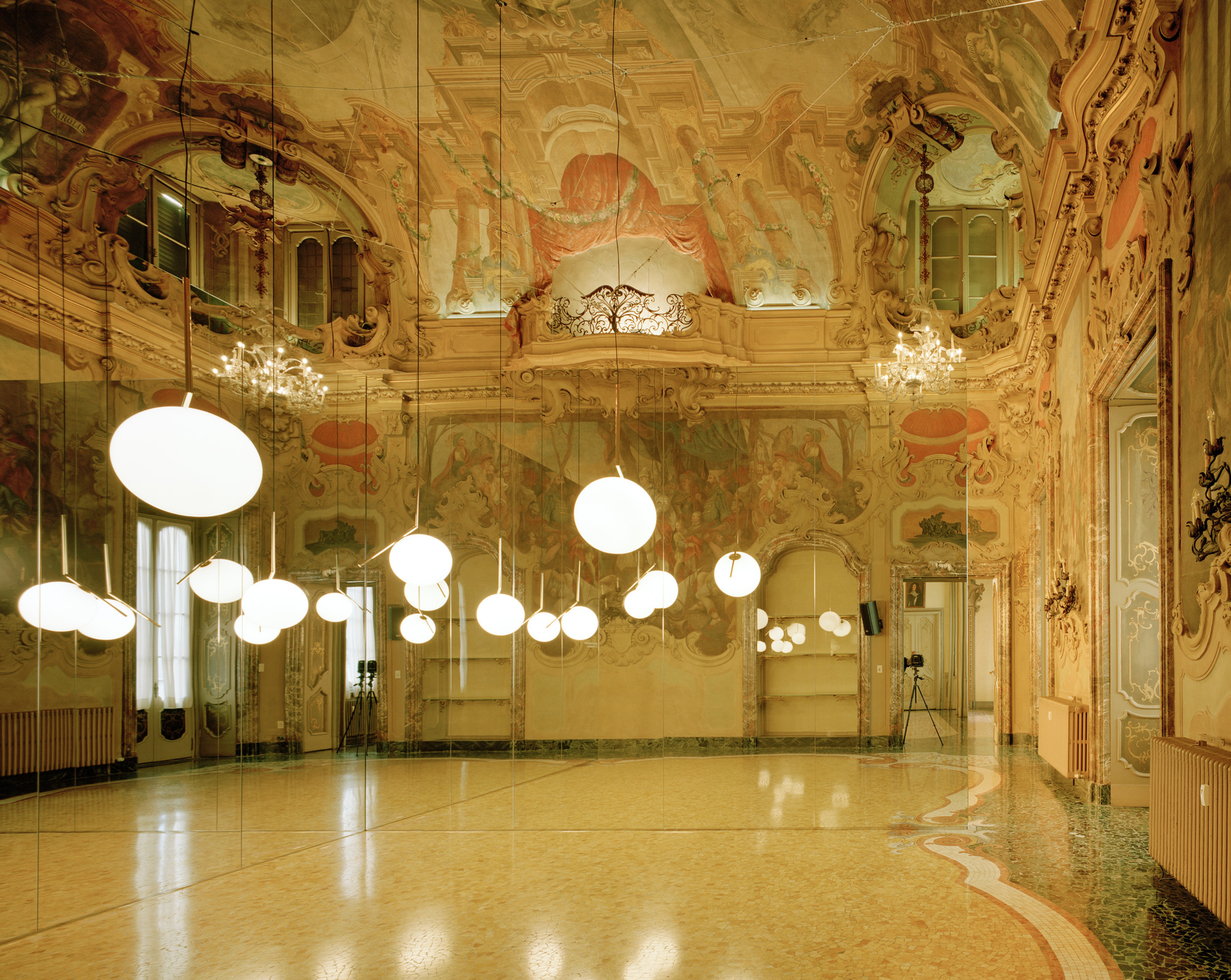 FLOS在2024米蘭設計週期間，選擇維斯孔蒂宮（Palazzo Visconti）這座米蘭巴洛克建築典範作為展示舞台。這棟建於17世紀的貴族宮殿，以其精雕細琢的立面設計與豪華 interior 聞名於世，堪稱米蘭巴洛克建築的巔峰之作。西班牙建築事務所ARQUITECTURA-G受邀打造特別裝置，呈現三位知名設計師的全新燈具系列，創造歷史建築與當代設計的精彩對話